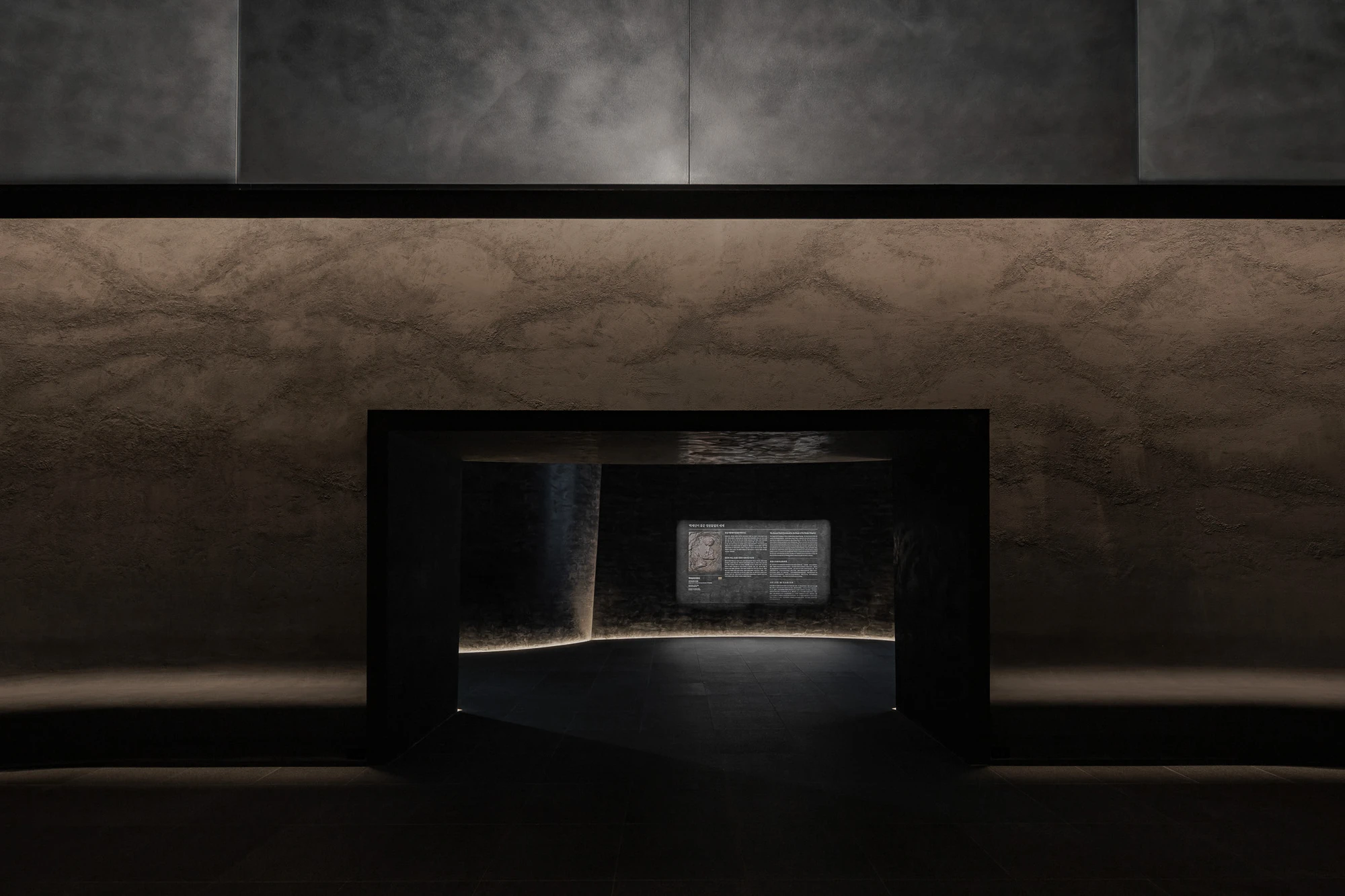 Baekje Gilt Bronze Incense Burner Hall (Buyeo National Museum) by WGNB — A darkened exhibition alcove houses a solitary illuminated display panel within a curved concrete envelope.