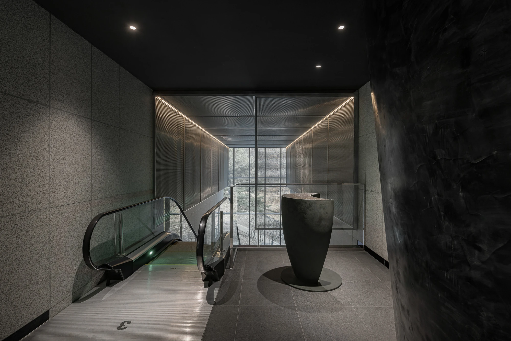 Baekje Gilt Bronze Incense Burner Hall (Buyeo National Museum) by WGNB — An escalator descends toward a monolithic black ceramic vessel positioned as the spatial anchor of the hall.