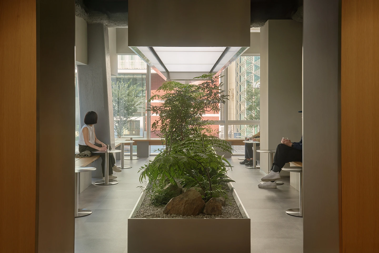 Alchemist Aoyama by Wynk Collaborative — A linear passage frames the interior garden as a focal point, with a central planter containing ferns and vegetation set against pale aggregate flooring.
