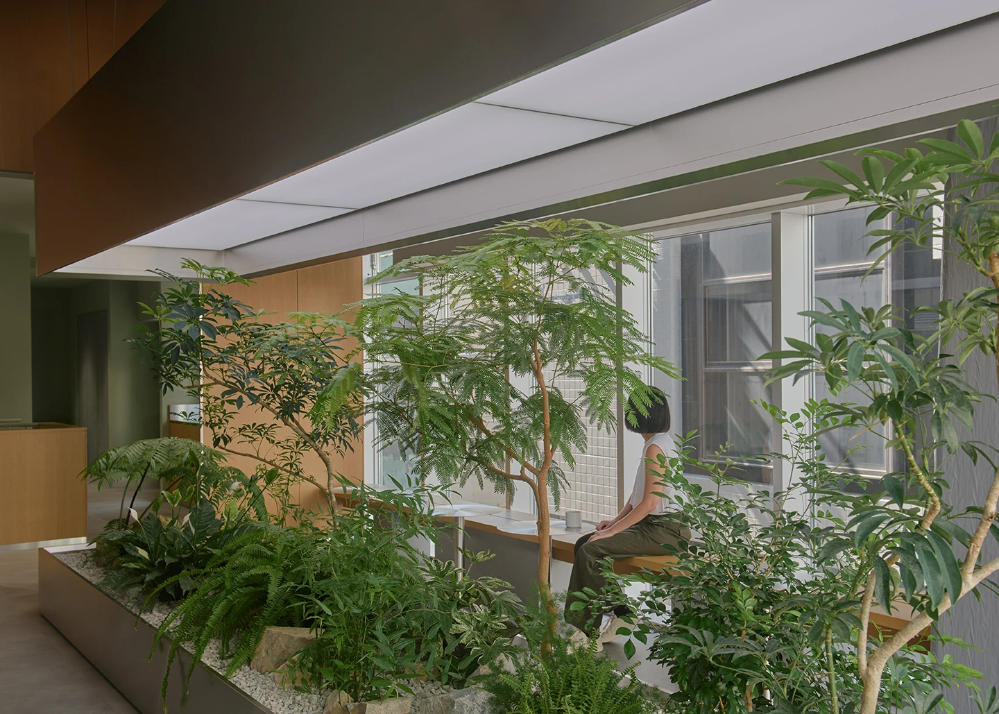 Alchemist Aoyama by Wynk Collaborative — A figure seated on an integrated bench observes the interior garden at Alchemist Aoyama.