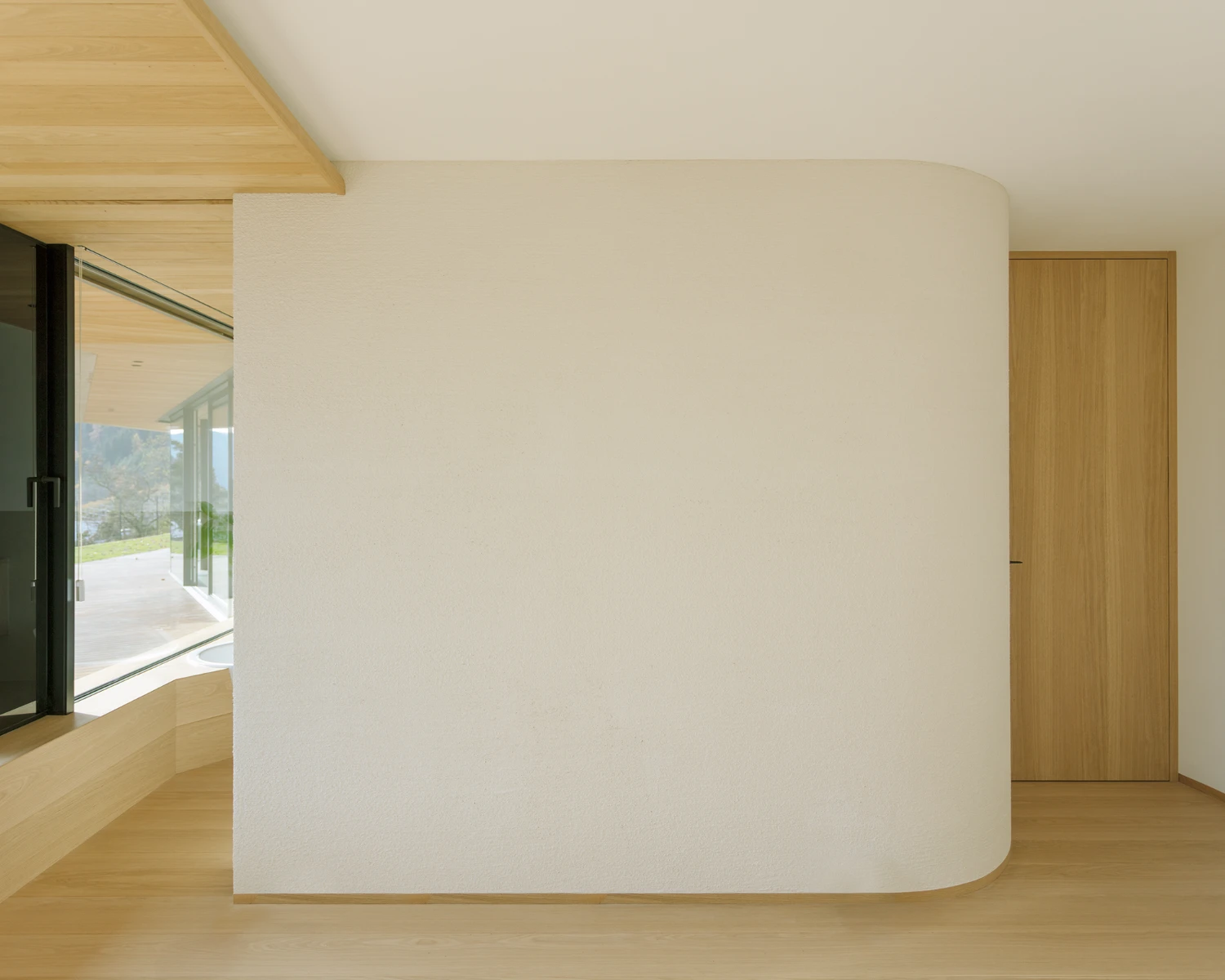Casa Conte by Messner Architects — A cream-rendered interior wall dominates the foreground, its curved corner detail softening the geometric volume.