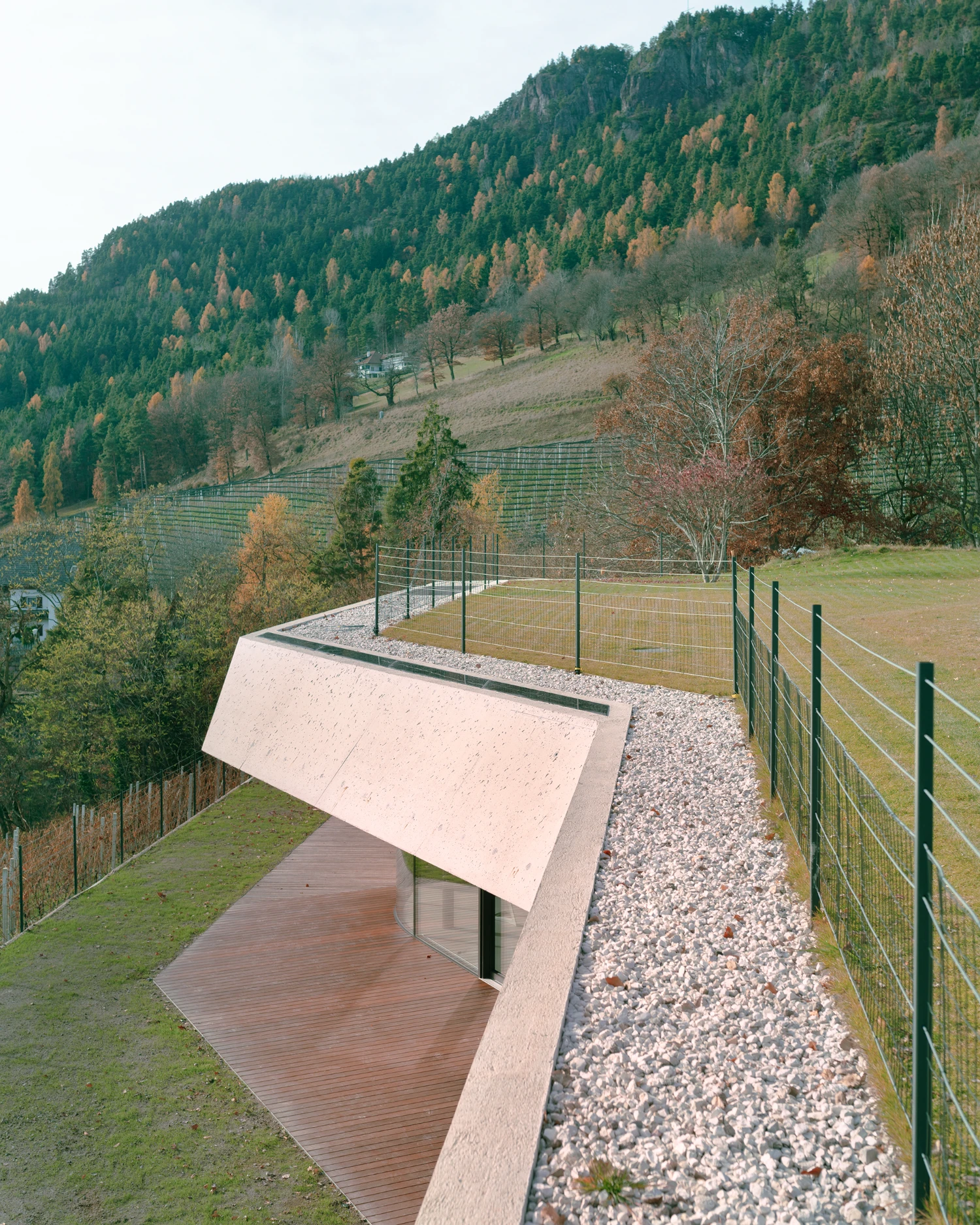 Casa Conte by Messner Architects — A concrete cantilever extends horizontally across the sloped terrain, its flat soffit creating a dramatic overhang above the timber-clad volume beneath.