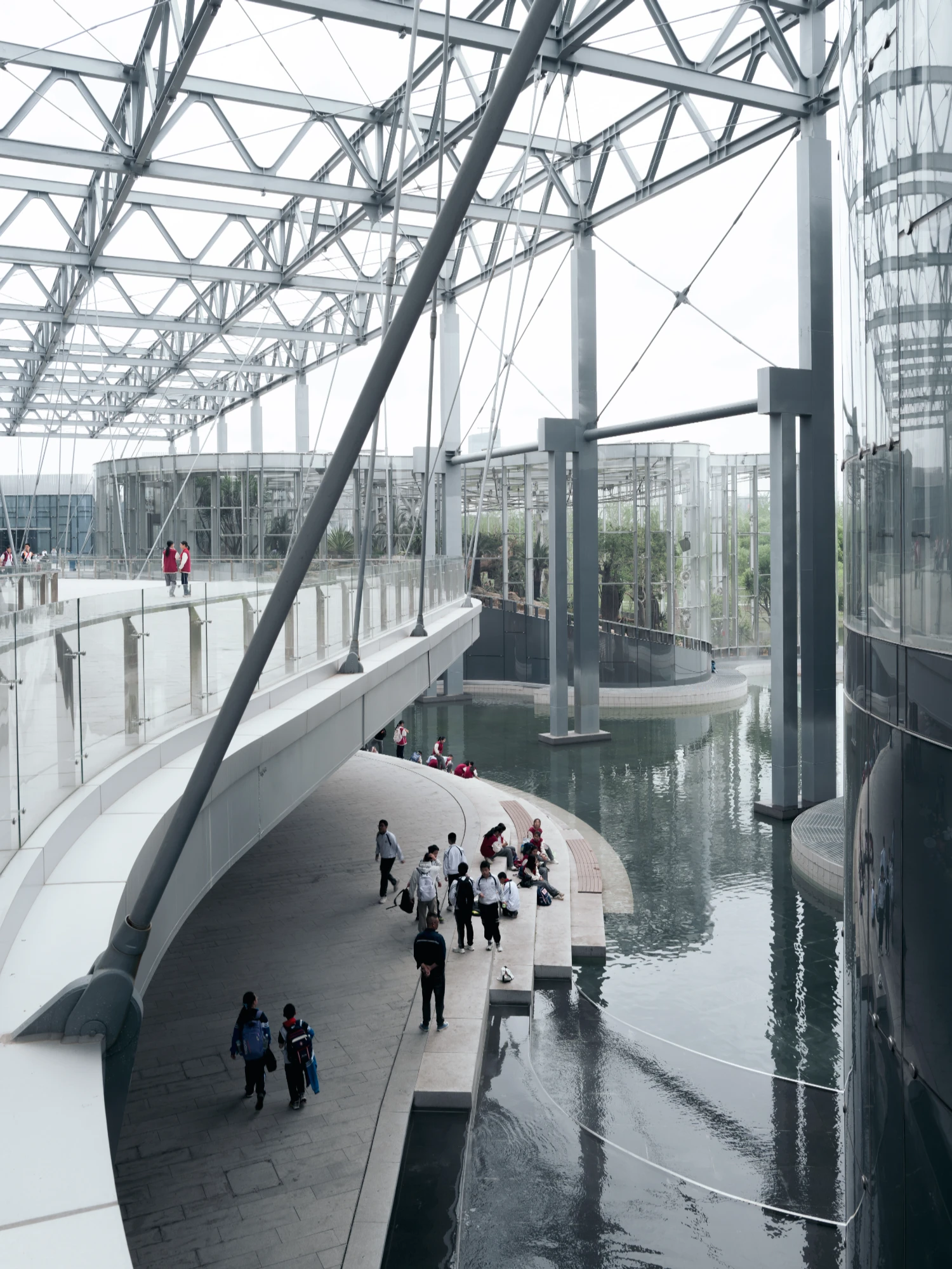 Expo Cultural Park Greenhouse Garden by Delugan Meissl captured by Marcus Yau — An elevated timber boardwalk curves alongside a water channel within a vast glazed greenhouse structure.