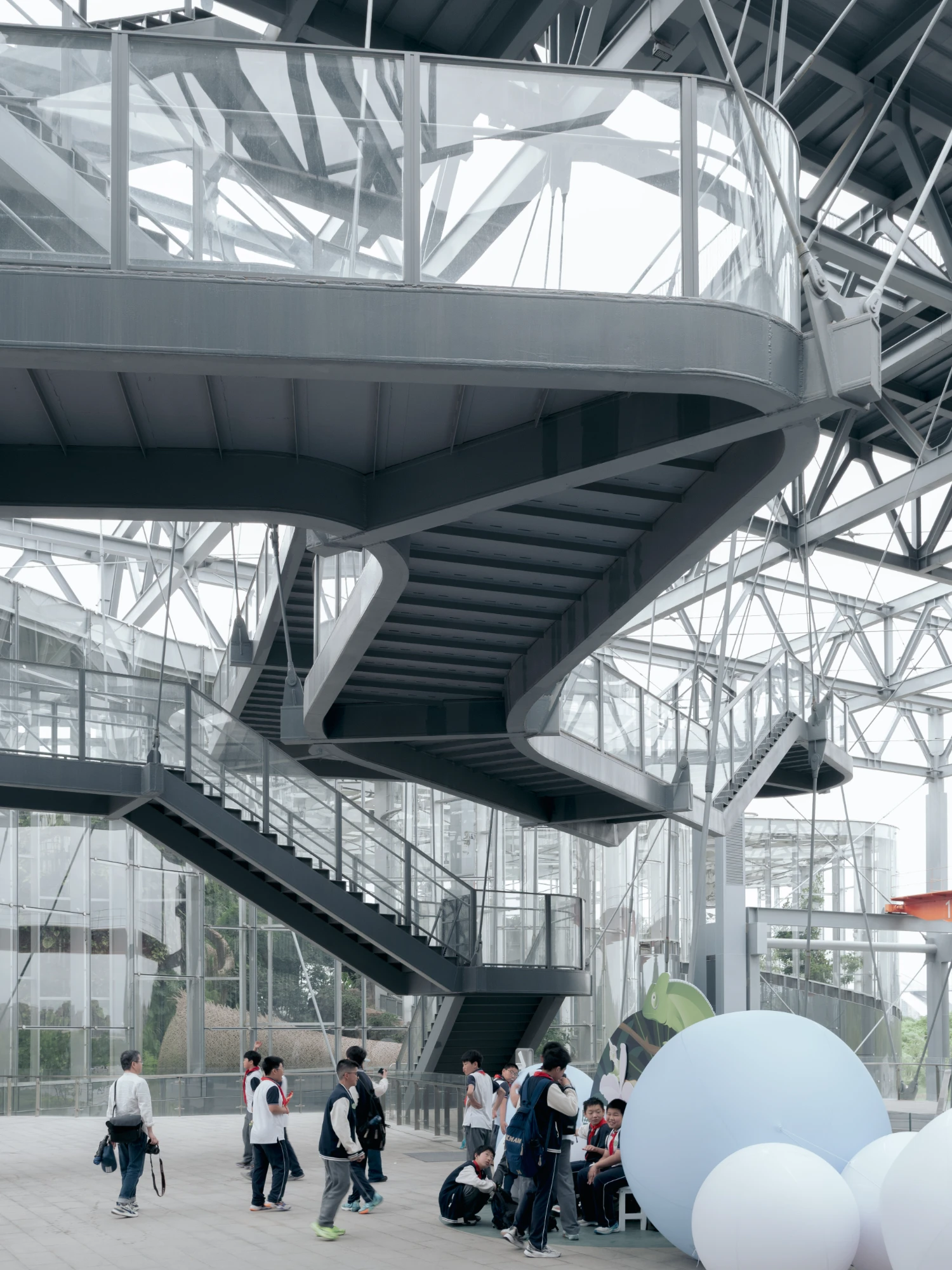 Expo Cultural Park Greenhouse Garden by Delugan Meissl captured by Marcus Yau — A spiraling steel staircase descends through a multi-level greenhouse structure, its dark treads contrasting against white steel railings and glass balustrades.