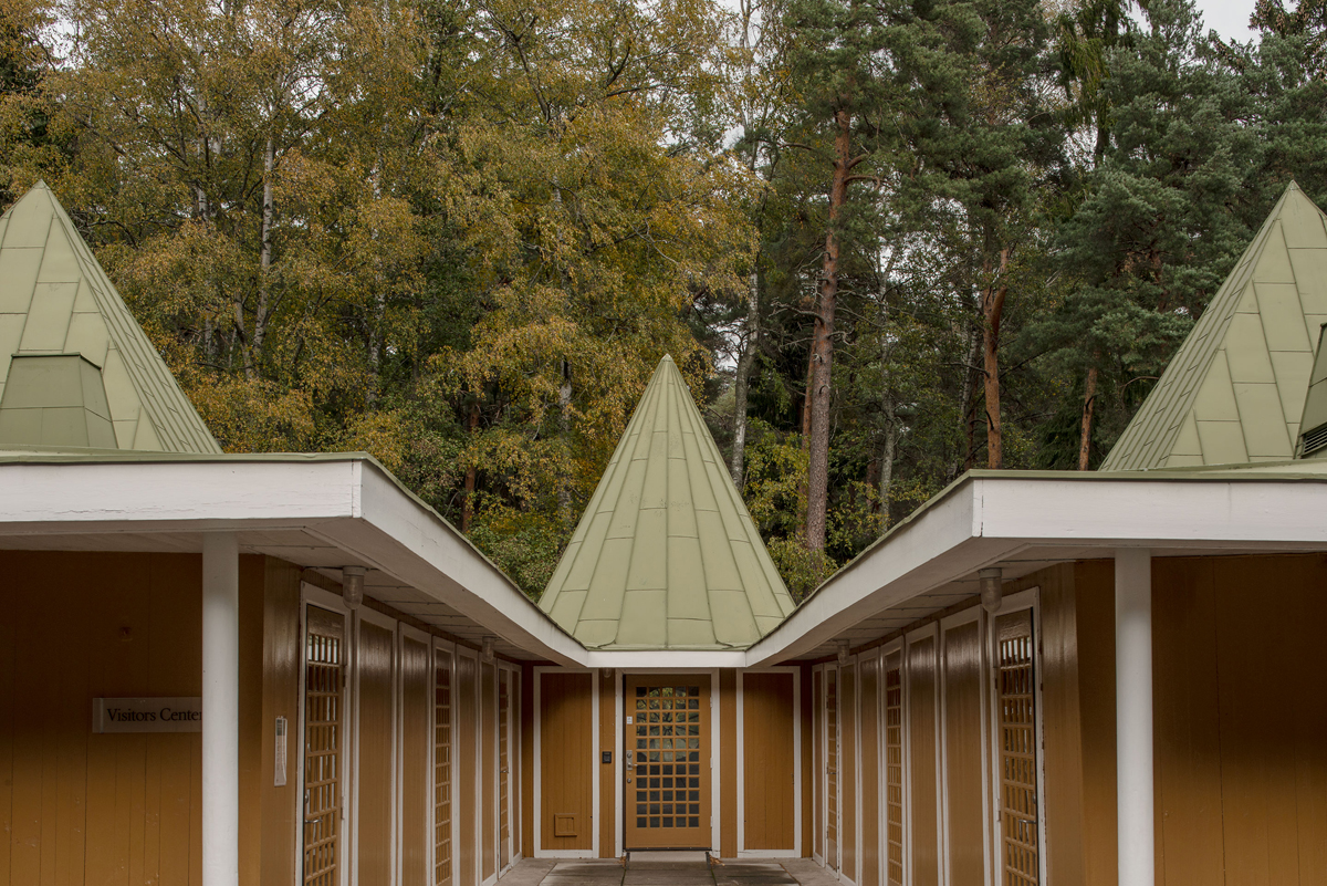 Woodland Cemetery Stockholm captured by Andy Liffner — A symmetrical pavilion structure within Woodland Cemetery's forest setting, featuring paired white-rendered wings with fluted pilasters flanking a central...