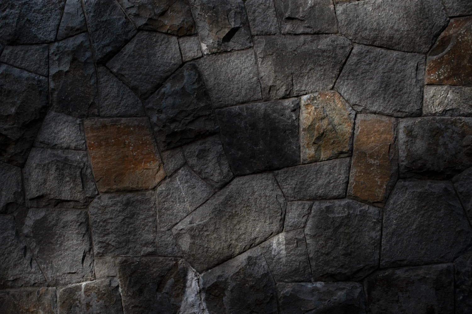 Woodland Cemetery Stockholm captured by Andy Liffner — Dry-laid stone masonry wall composed of predominantly dark granite blocks in irregular coursing, with occasional rust-toned stones interspersed throughout.