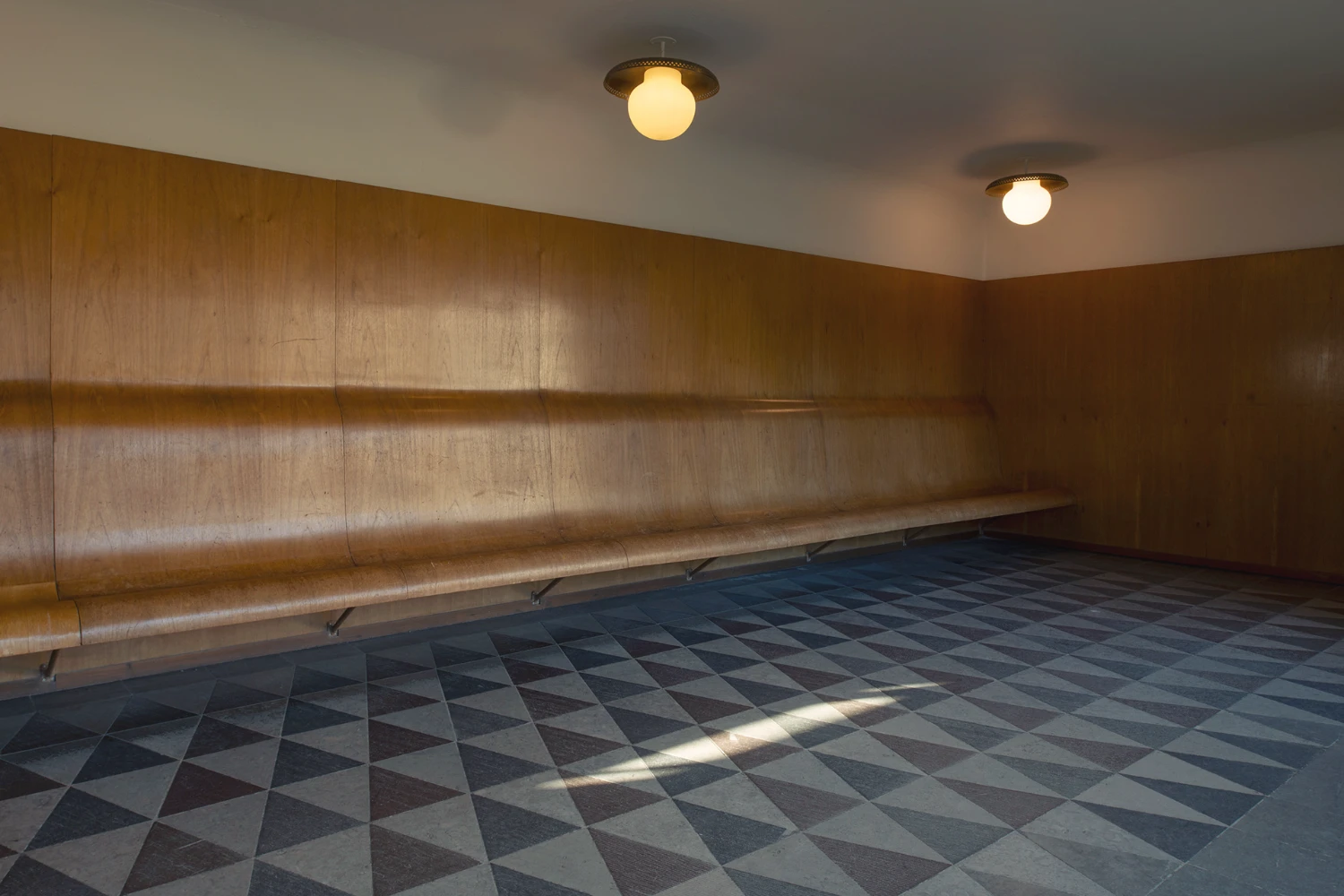 Woodland Cemetery Stockholm captured by Andy Liffner — A vaulted corridor within Woodland Cemetery's chapel complex, lined with timber wall paneling in warm oak tones.