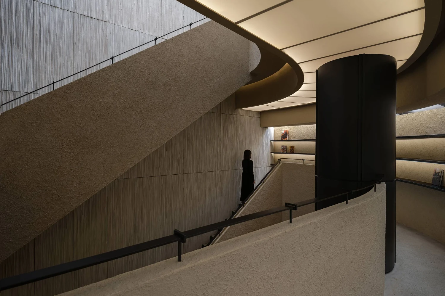 The Graphic bookstore by OONN Metaworks + U.LAB — A multi-level interior passage descends through a cylindrical concrete column, its monolithic form anchoring the composition.
