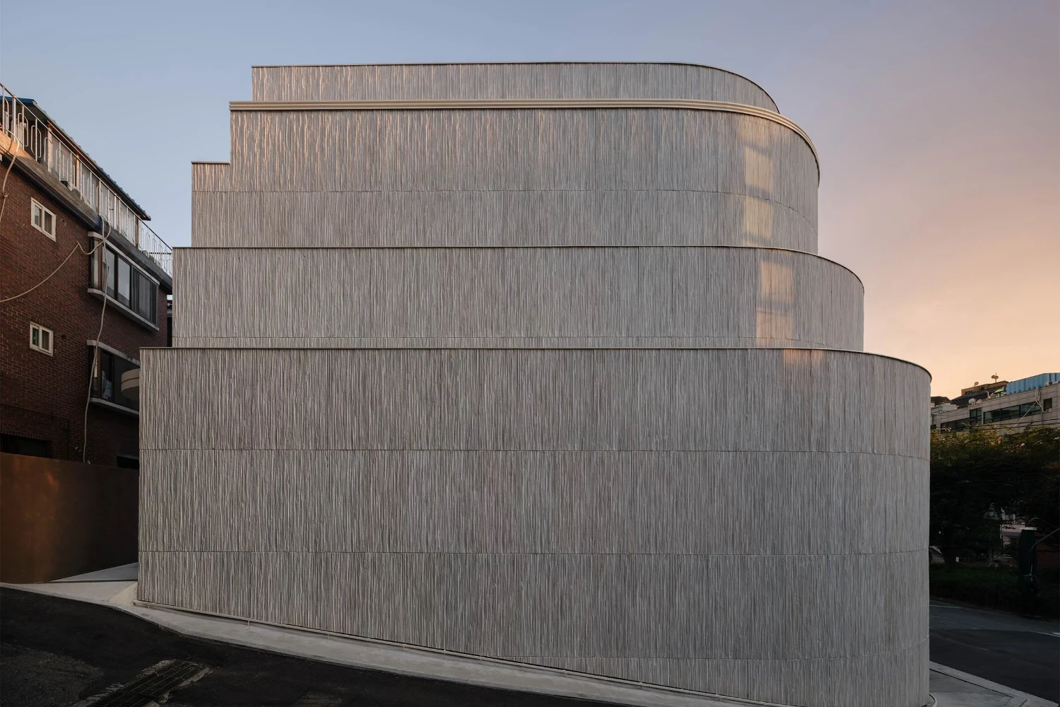 The Graphic bookstore by OONN Metaworks + U.LAB — The Graphic bookstore presents a cylindrical volume clad in horizontal corrugated metal bands, its weathered surface catching golden-hour light across a...