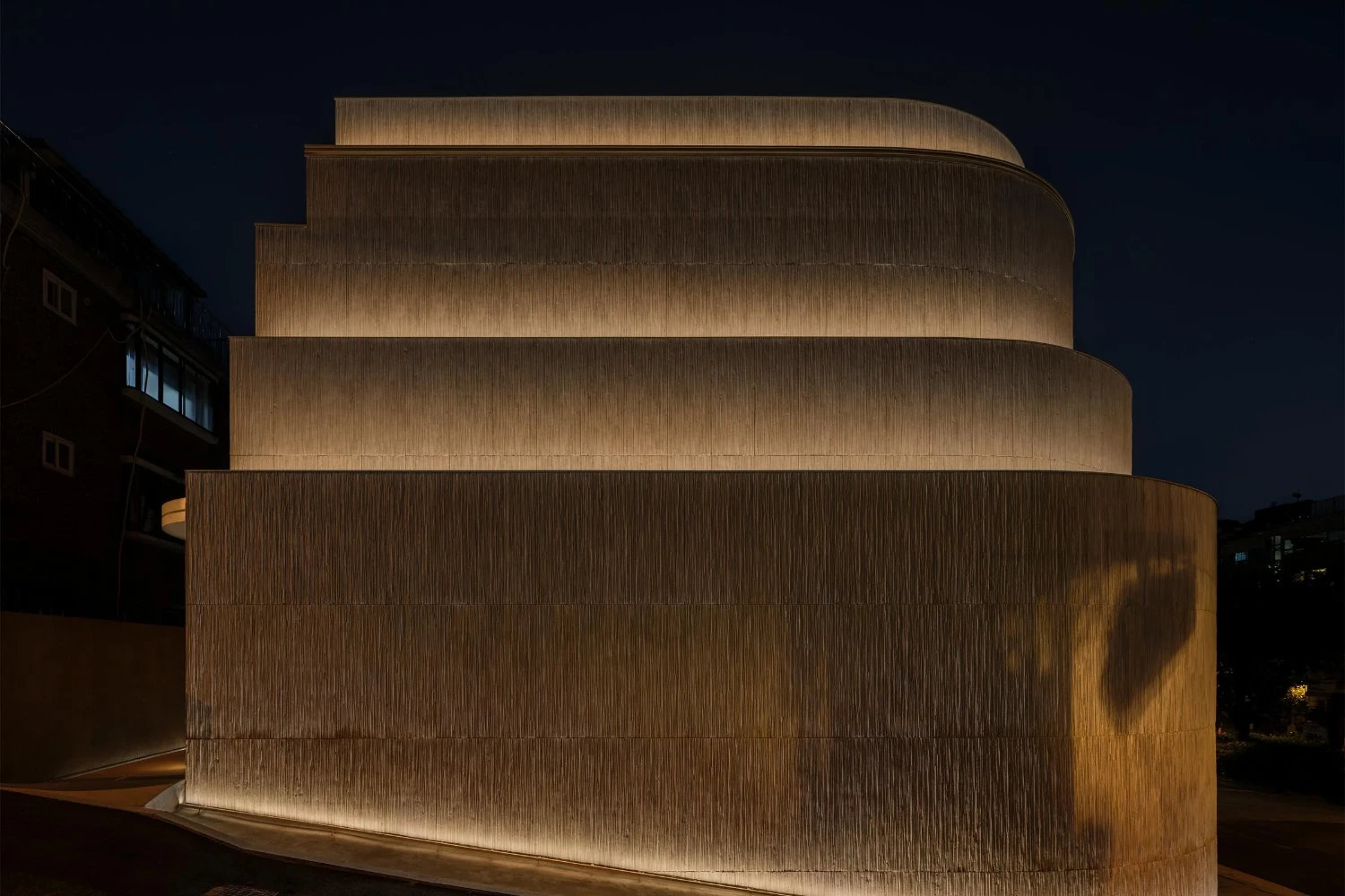 The Graphic bookstore by OONN Metaworks + U.LAB — Evening photograph of The Graphic bookstore reveals its cylindrical massing through stacked horizontal sections that recede toward the crown.