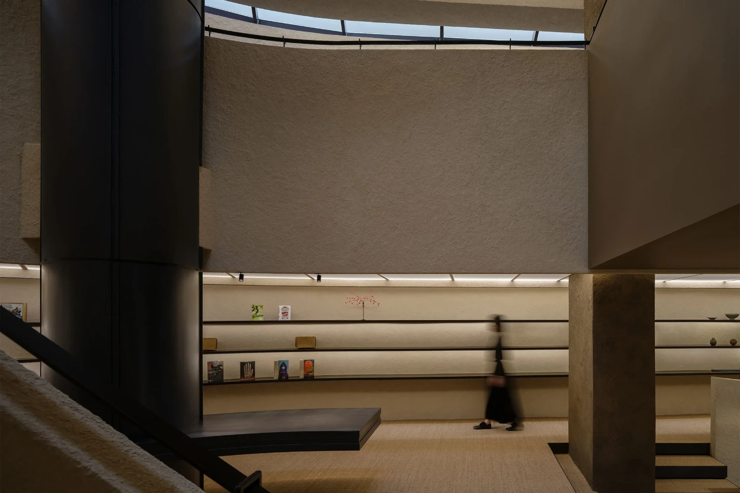 The Graphic bookstore by OONN Metaworks + U.LAB — Interior view of a multi-level gallery space with continuous horizontal shelving recessed into the cream-colored rear wall.