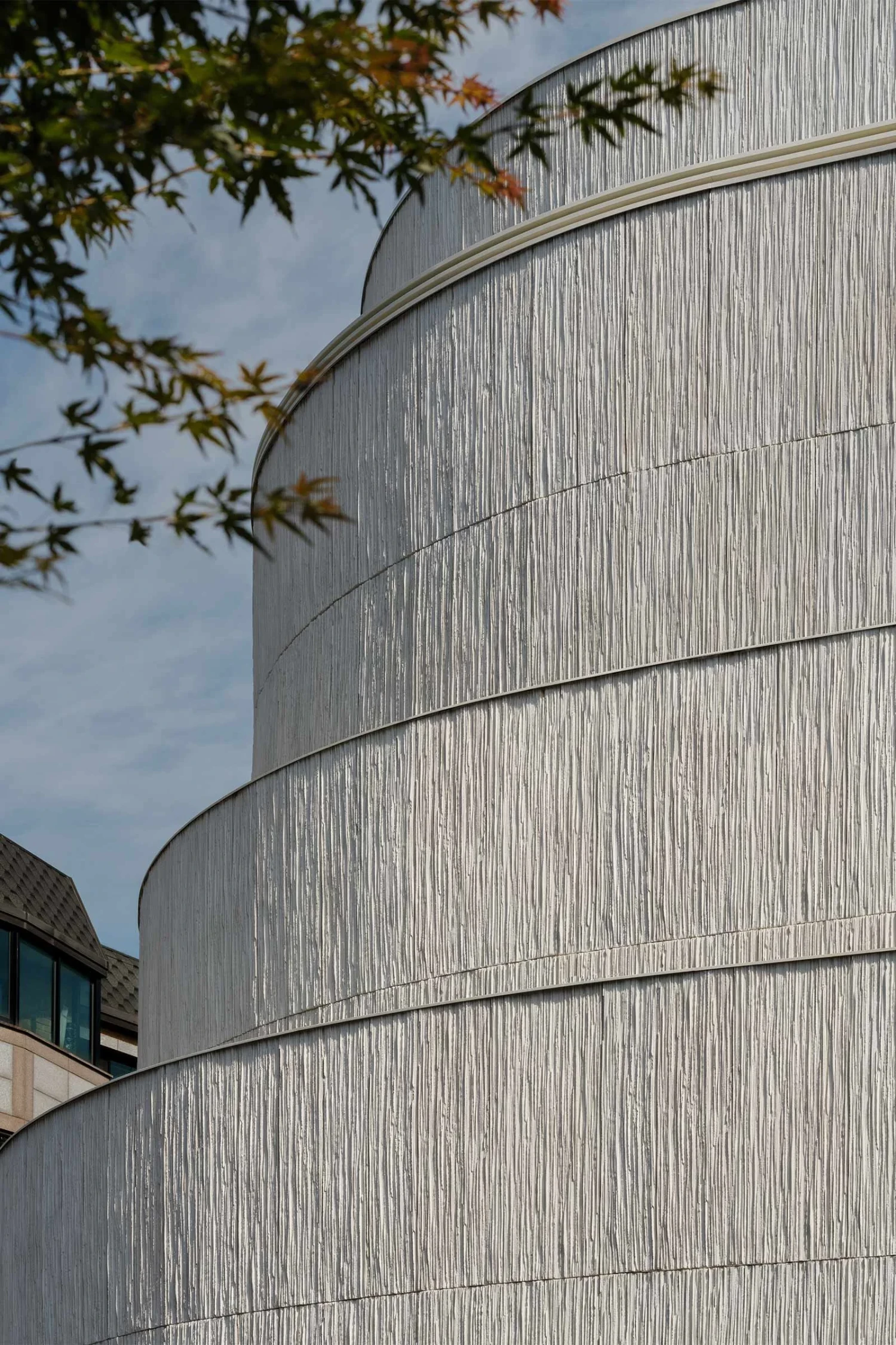 The Graphic bookstore by OONN Metaworks + U.LAB — The cylindrical volume dominates the frame, its surface articulated by horizontal corrugated metal bands stacked in graduated tiers.
