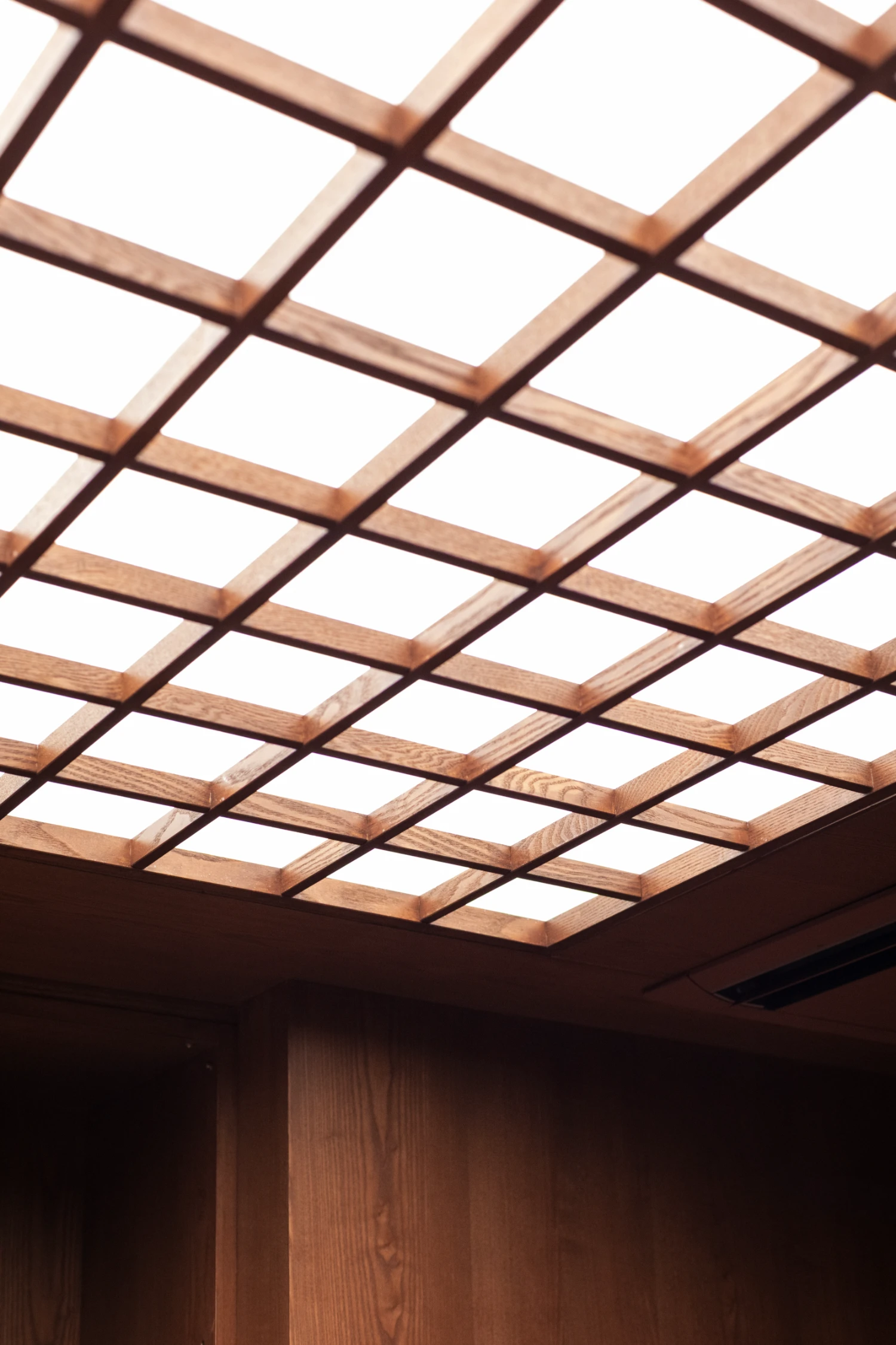 uru coffee by TRANSFORM — Overhead view of a timber lattice ceiling with regular square openings, creating a geometric grid pattern against bright sky.