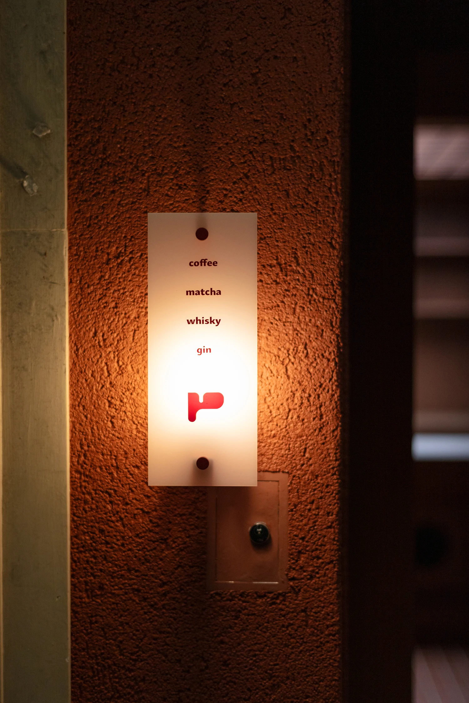 uru coffee by TRANSFORM — A illuminated signage panel mounted on a textured terracotta render wall functions as wayfinding for uru coffee.