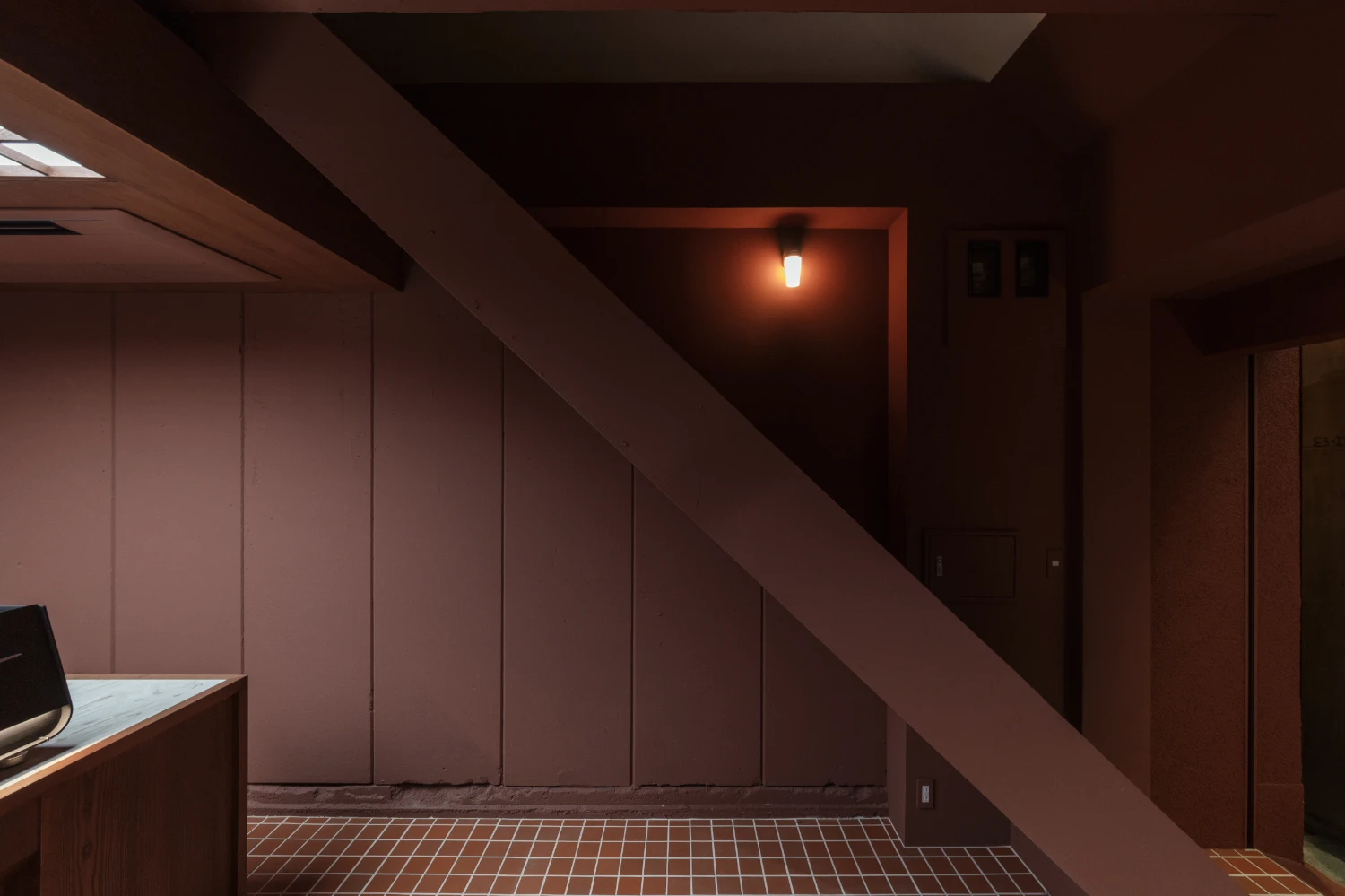 uru coffee by TRANSFORM — A staircase descends diagonally across the frame, its timber handrail cutting through terracotta-walled space.