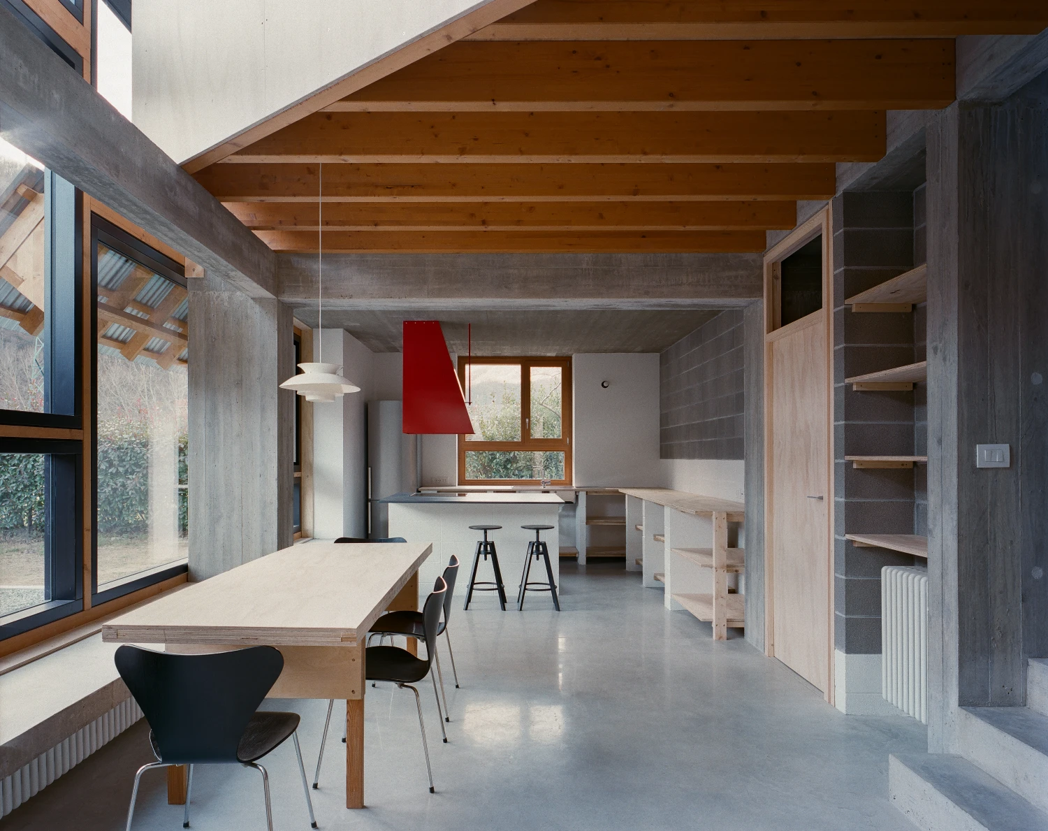 Casa BM by ErranteArchitetture — The kitchen pavilion opens to a continuous interior volume through full-height glazing, its exposed timber beam ceiling articulating the spatial hierarchy.
