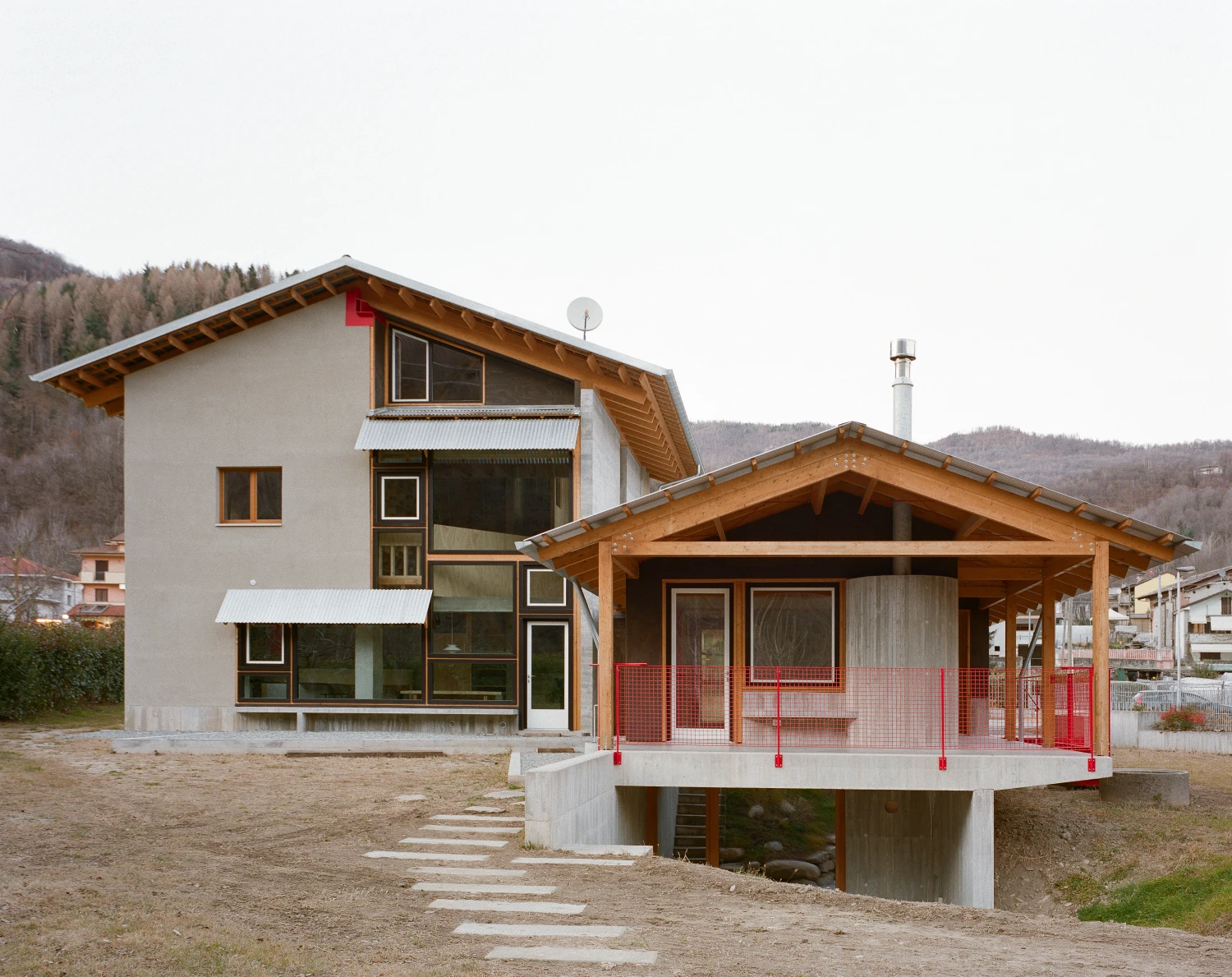 Casa BM by ErranteArchitetture — The pavilion extension dominates this view, its timber-framed gable cantilevered over a concrete platform elevated on pilotis.