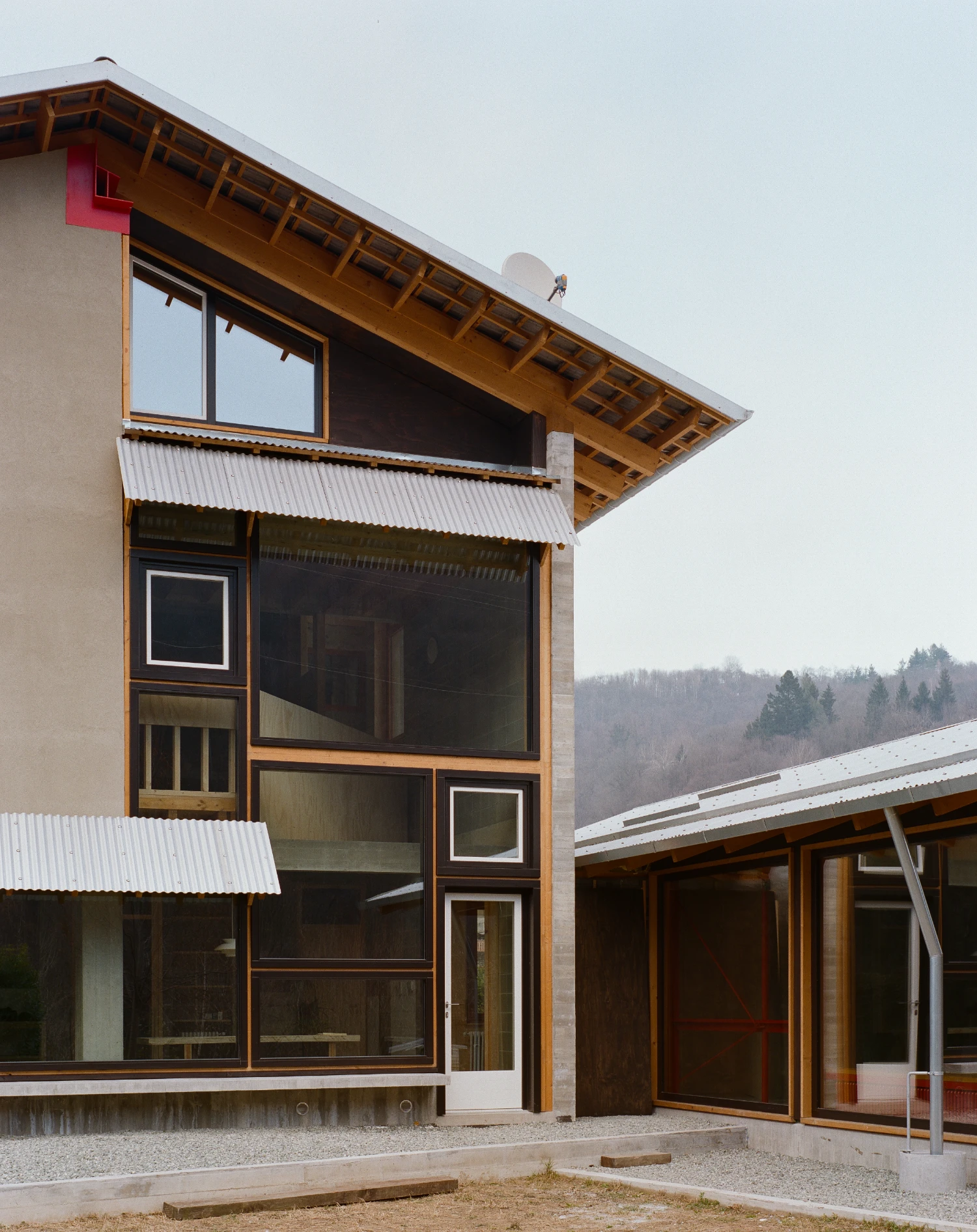 Casa BM by ErranteArchitetture — A timber-framed pavilion extension with exposed beam structure and deep overhang dominates the composition, its wooden skeleton articulated against the pale...