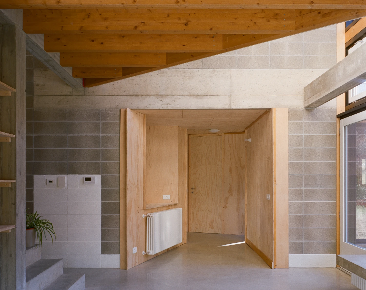 Casa BM by ErranteArchitetture — Interior passage framed by large timber-clad structural box defining a threshold between concrete and wood.