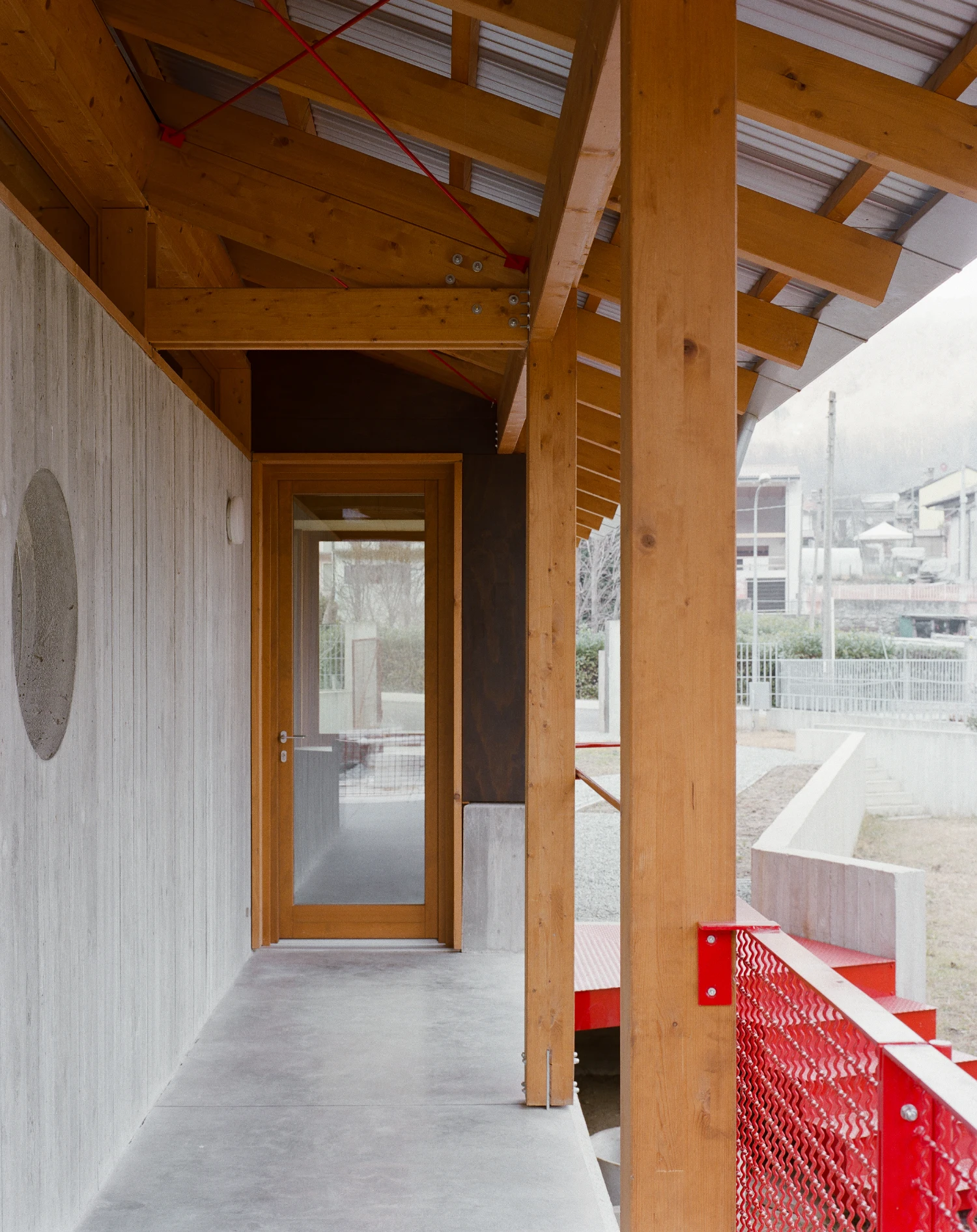 Casa BM by ErranteArchitetture — A covered passage frames the entry to Casa BM, defined by post-and-beam timber structure with exposed joinery and deep overhang.