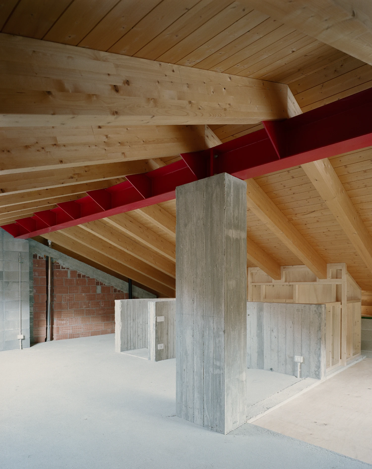 Casa BM by ErranteArchitetture — An interior attic space under construction reveals the project's structural logic: exposed pine timber beams and boarding span the pitched ceiling, while a...