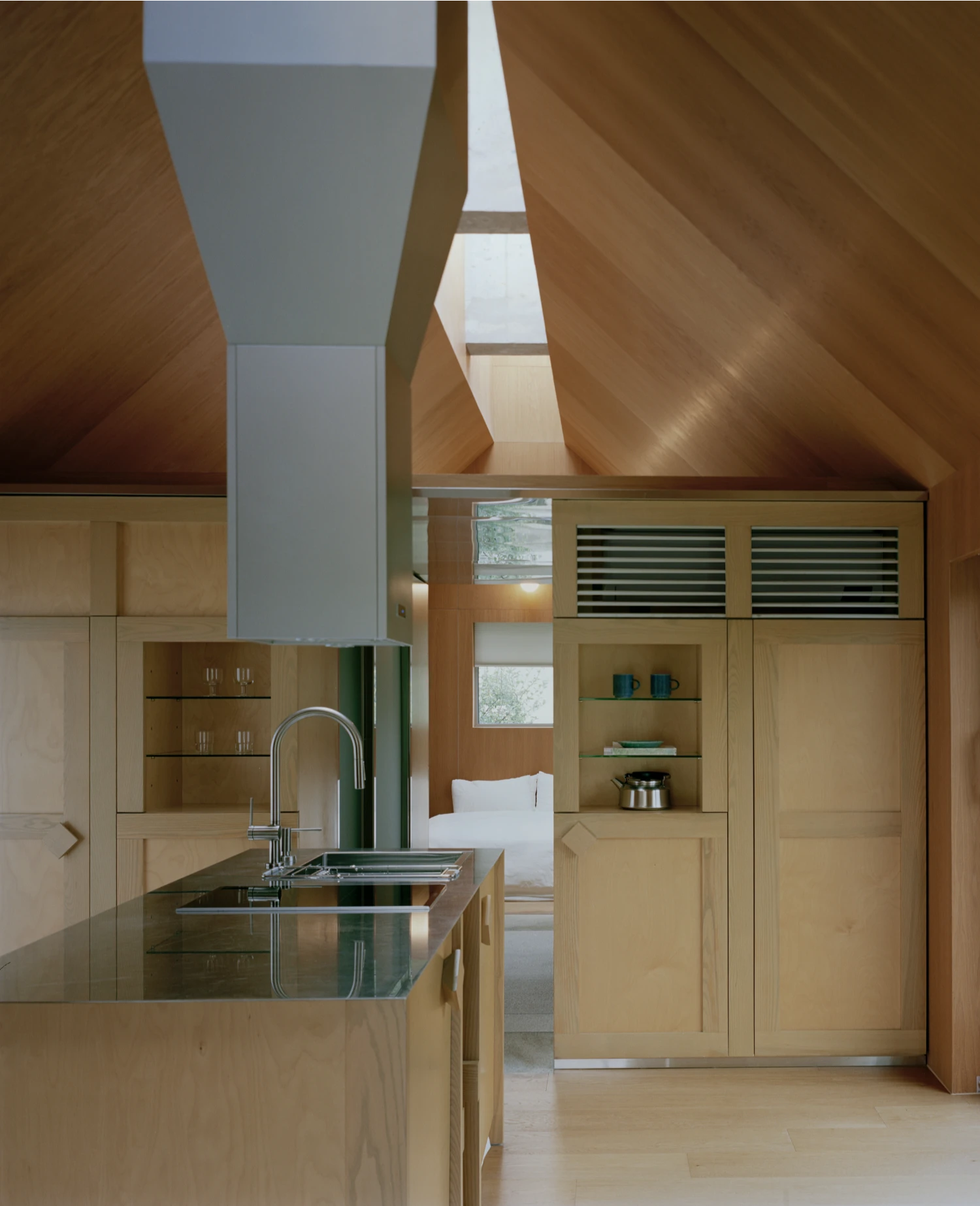 Hoji Gangneung Houses by AOA Architects captured by Danny Kai — Interior view of a timber-lined kitchen and living space beneath a dramatically angled roof plane.