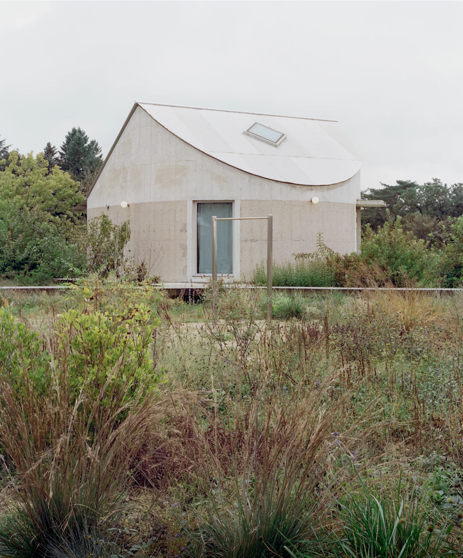 Hoji Gangneung Houses by AOA Architects captured by Danny Kai — A rendered concrete dwelling sits elevated on a concrete plinth, its faceted roof plane cutting a geometric silhouette against an overcast sky.