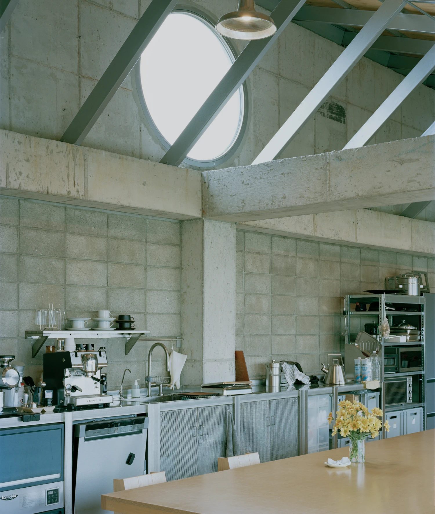 Hoji Gangneung Houses by AOA Architects captured by Danny Kai — Kitchen interior beneath a faceted concrete ceiling with circular skylight and suspended brass pendant.