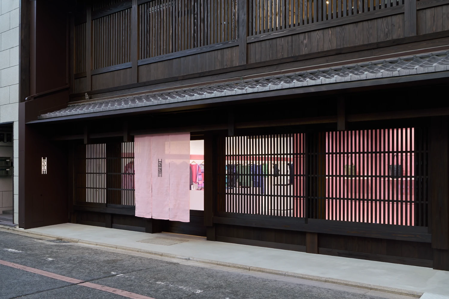 Issey Miyake HaaT flagship in Kyoto by Tokujin Yoshioka — The street-level facade of Issey Miyake HaaT presents a restrained composition of charcoal timber lattice screens interrupted by a centered pale pink noren...