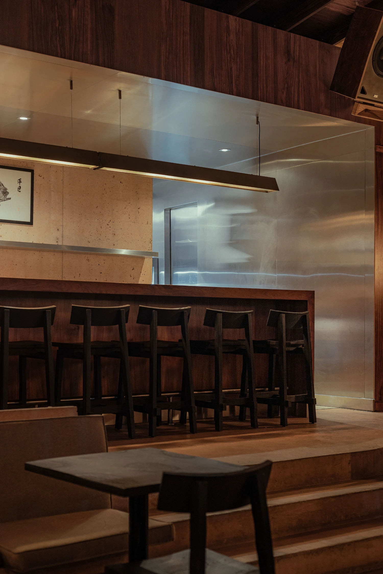 ZUKE Restaurant by Sofía Betancur + Taller Nacional — The sushi counter at ZUKE occupies a raised platform defined by brushed steel cylindrical elements and dark timber framing.