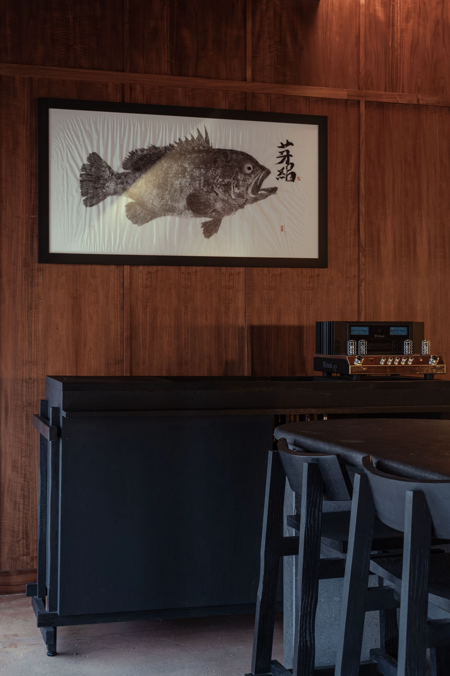 ZUKE Restaurant by Sofía Betancur + Taller Nacional — A framed Japanese ink drawing of a fish dominates the wood-paneled wall, its monochromatic rendering echoing the interior's restrained palette.
