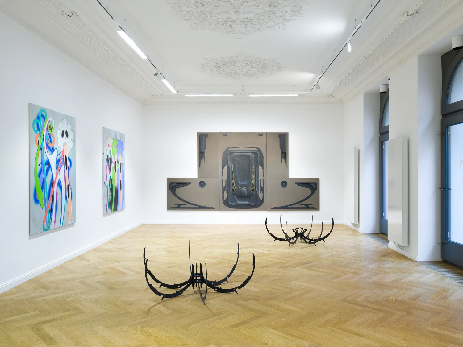 Bloom by Tomáš Absolon Milan Vagač at SPOT Gallery — SPOT Gallery's white-walled interior showcases a triptych wall installation depicting an overhead car perspective in dark tones against beige ground,...