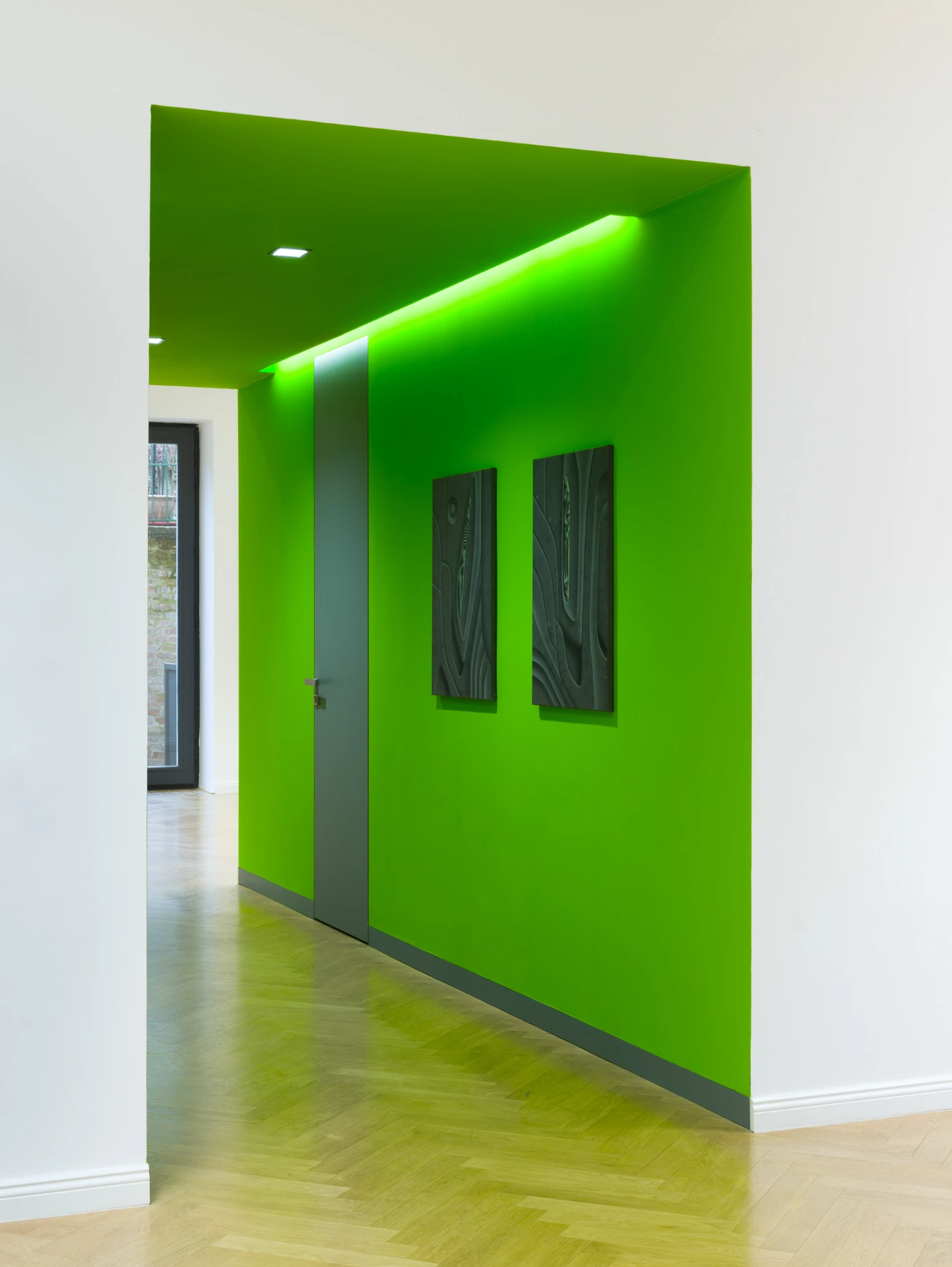 Bloom by Tomáš Absolon Milan Vagač at SPOT Gallery — A lime-green corridor wall anchors the gallery passage, its saturated surface interrupted by a dark steel vertical divider and two black framed works...