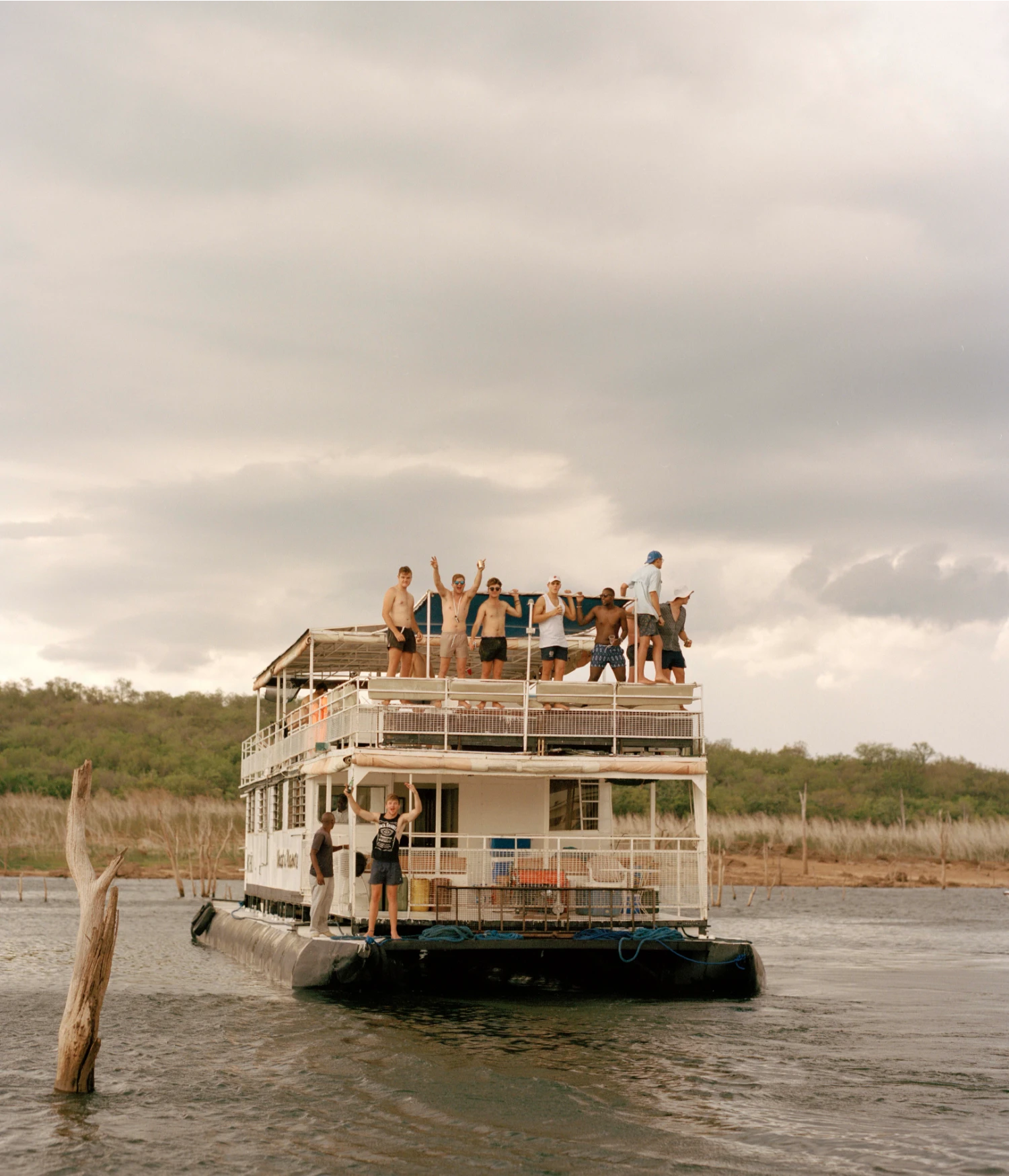 They Still Owe Him a Boat by Jono Terry — A multi-story floating structure anchored in the Zambezi Valley waters, its white-painted timber frame and metal railings rising against an overcast sky.
