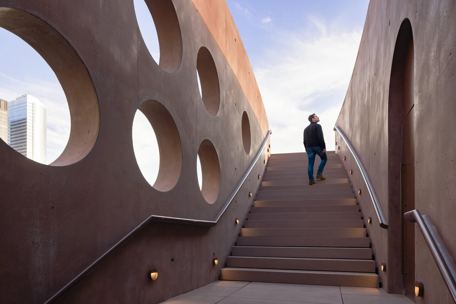 Wagner Park Pavilion by Thomas Phifer — A visitor ascends a monolithic concrete staircase framed by curved archways that define Wagner Park Pavilion's monumental gateway.