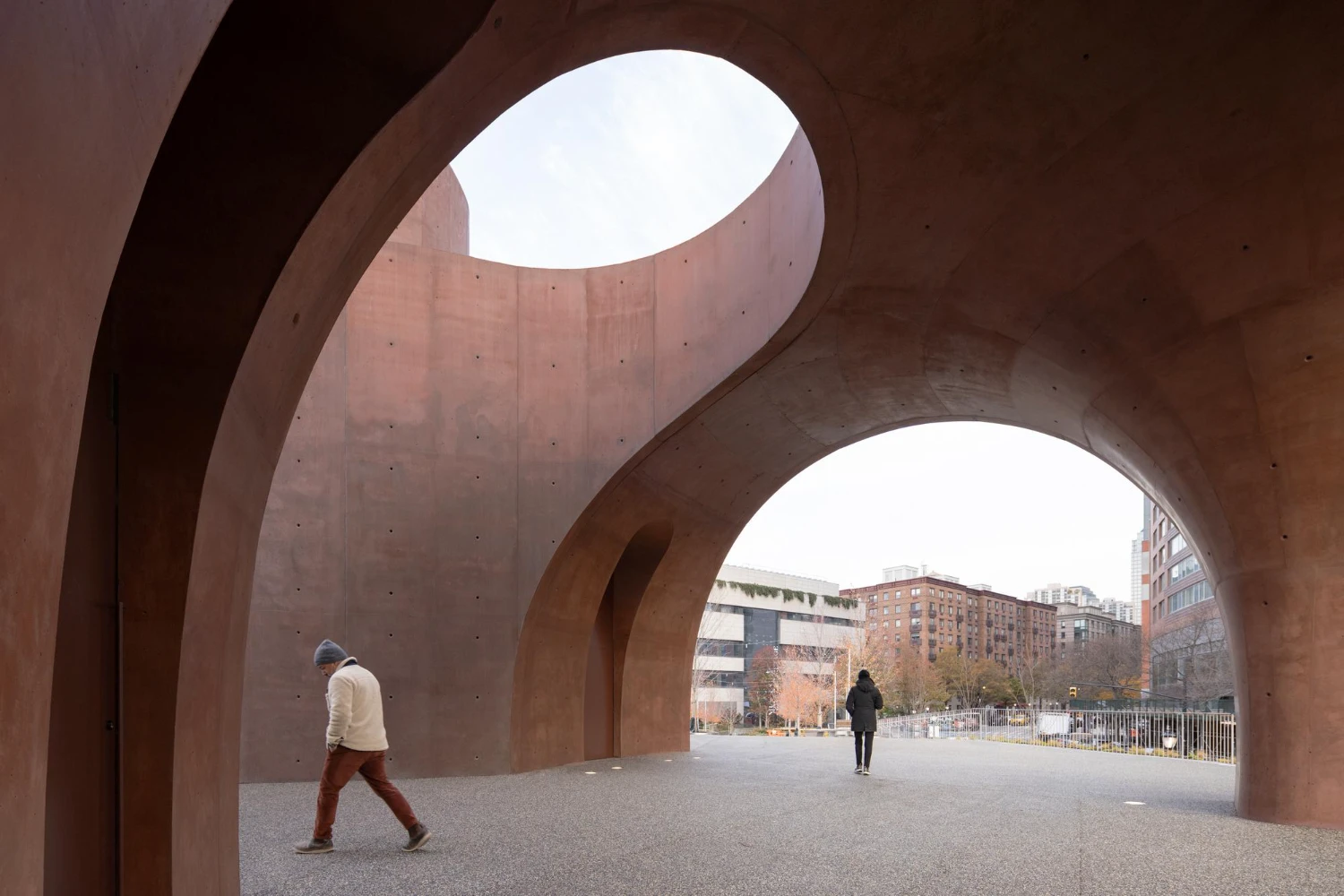 Wagner Park Pavilion by Thomas Phifer — Twin monolithic concrete arches frame a gateway void at Wagner Park Pavilion, their reddish-brown surfaces revealing formwork fastener holes in a regular grid.