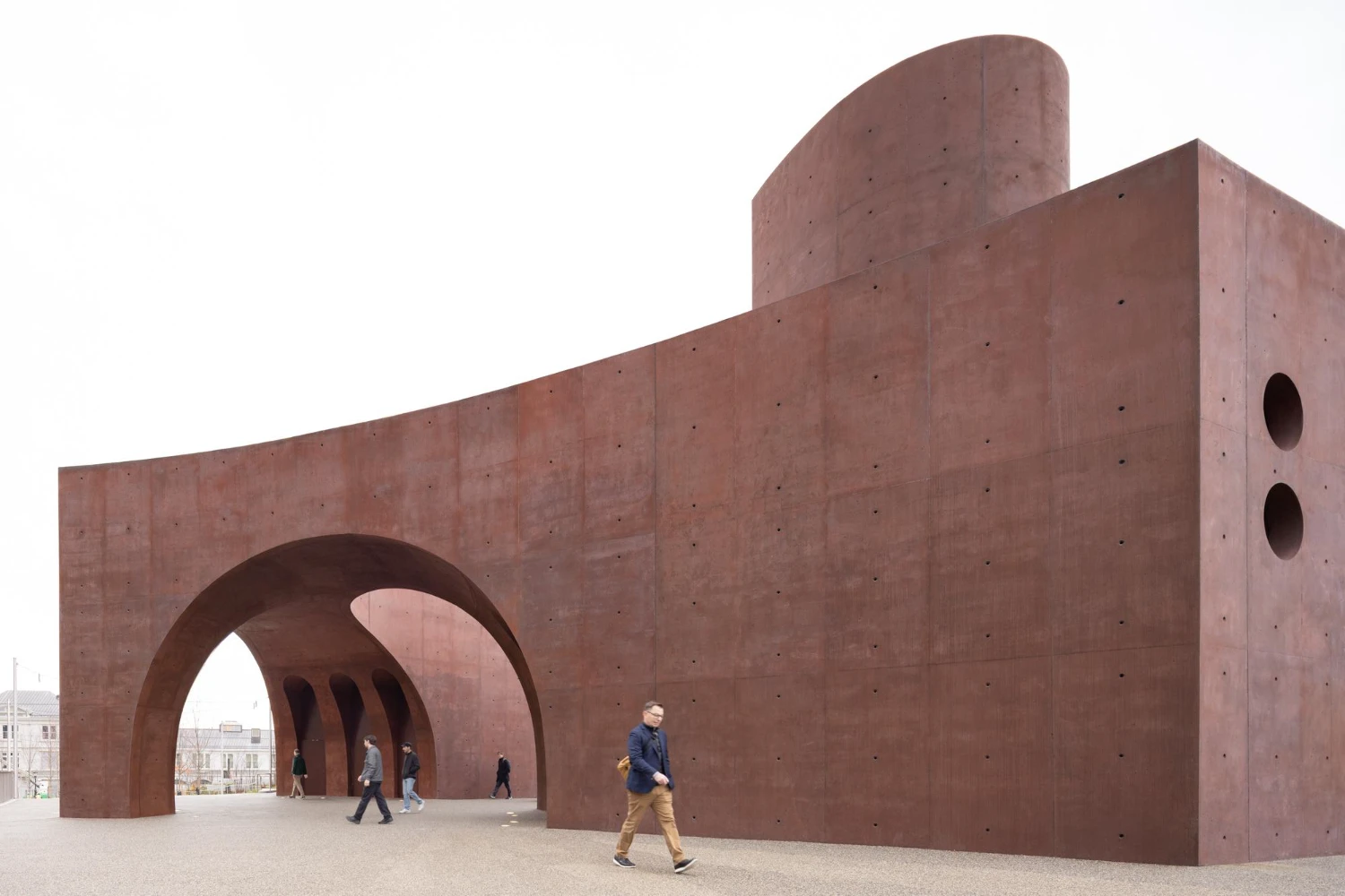 Wagner Park Pavilion by Thomas Phifer — Twin monumental concrete arches frame a pedestrian gateway at Wagner Park Pavilion, their curved forms casting deep shadows across the sand-colored ground...