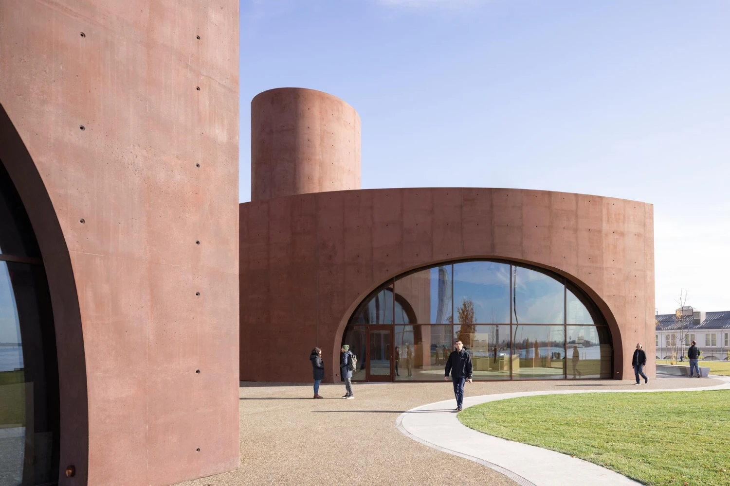 Wagner Park Pavilion by Thomas Phifer — The pavilion's monumental double arch dominates the composition, its reddish-brown concrete surface marked by regular fastener holes from board-formed casting.