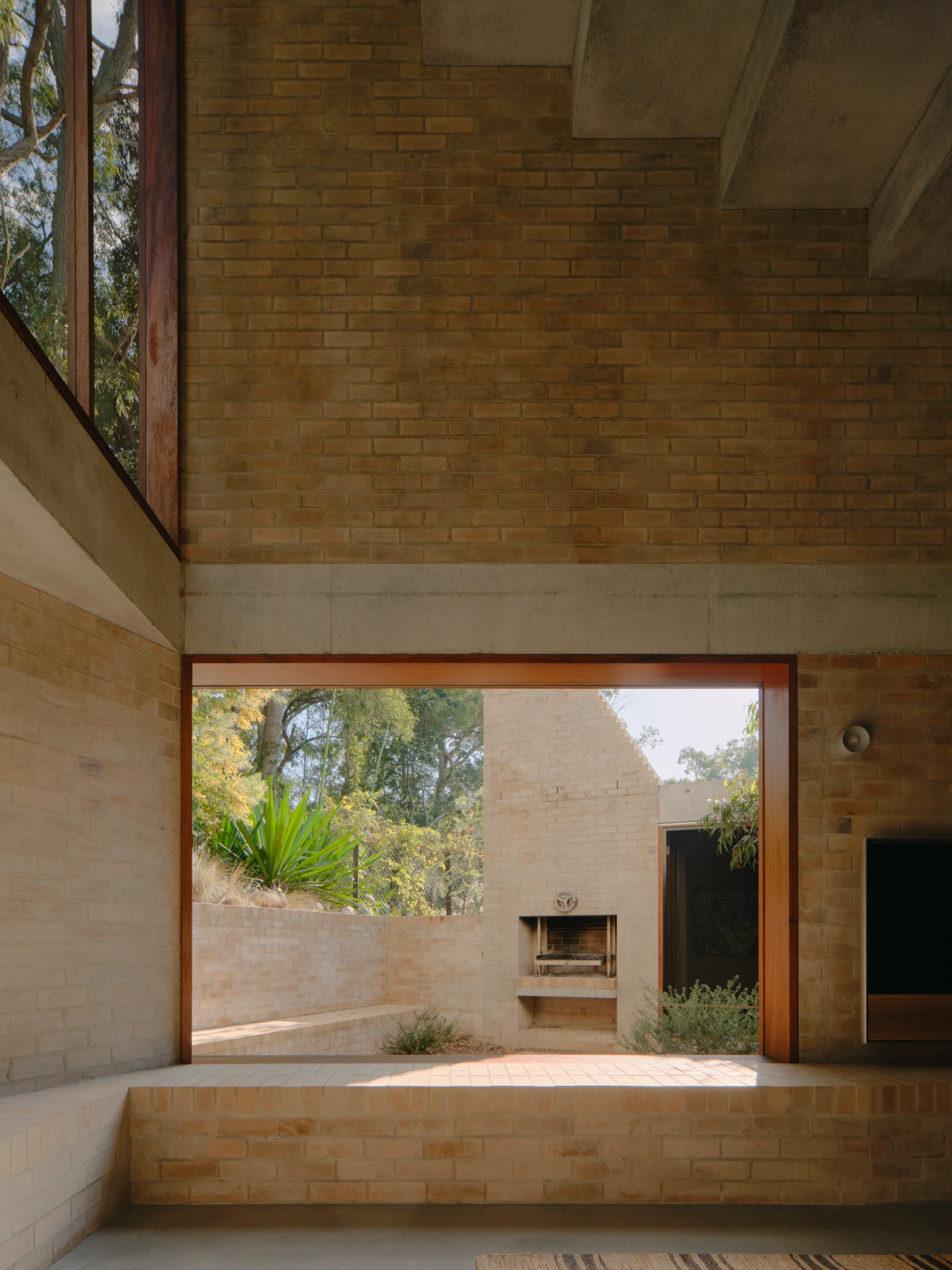 Stuartholme House by Nielsen Jenkins + Michael Lumby — A timber-framed aperture opens from the brick interior onto a sunlit courtyard, establishing a threshold between built and landscape zones.