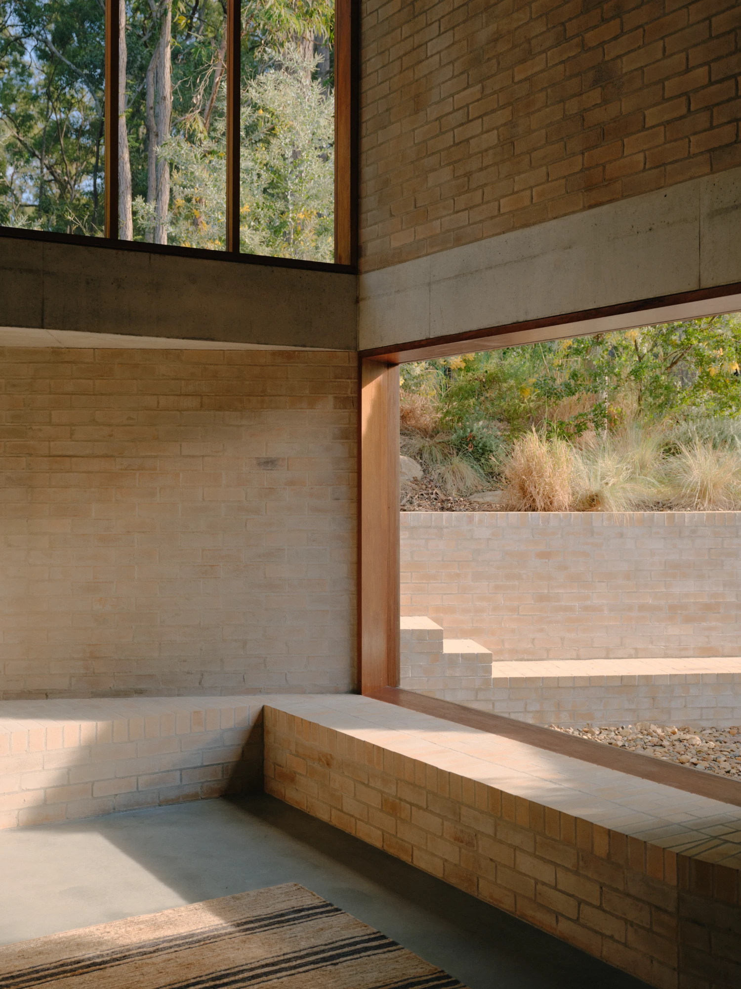 Stuartholme House by Nielsen Jenkins + Michael Lumby — A sunken interior volume lined in warm brick establishes a recessed floor plane that visually anchors the space into the landscaped gully beyond.