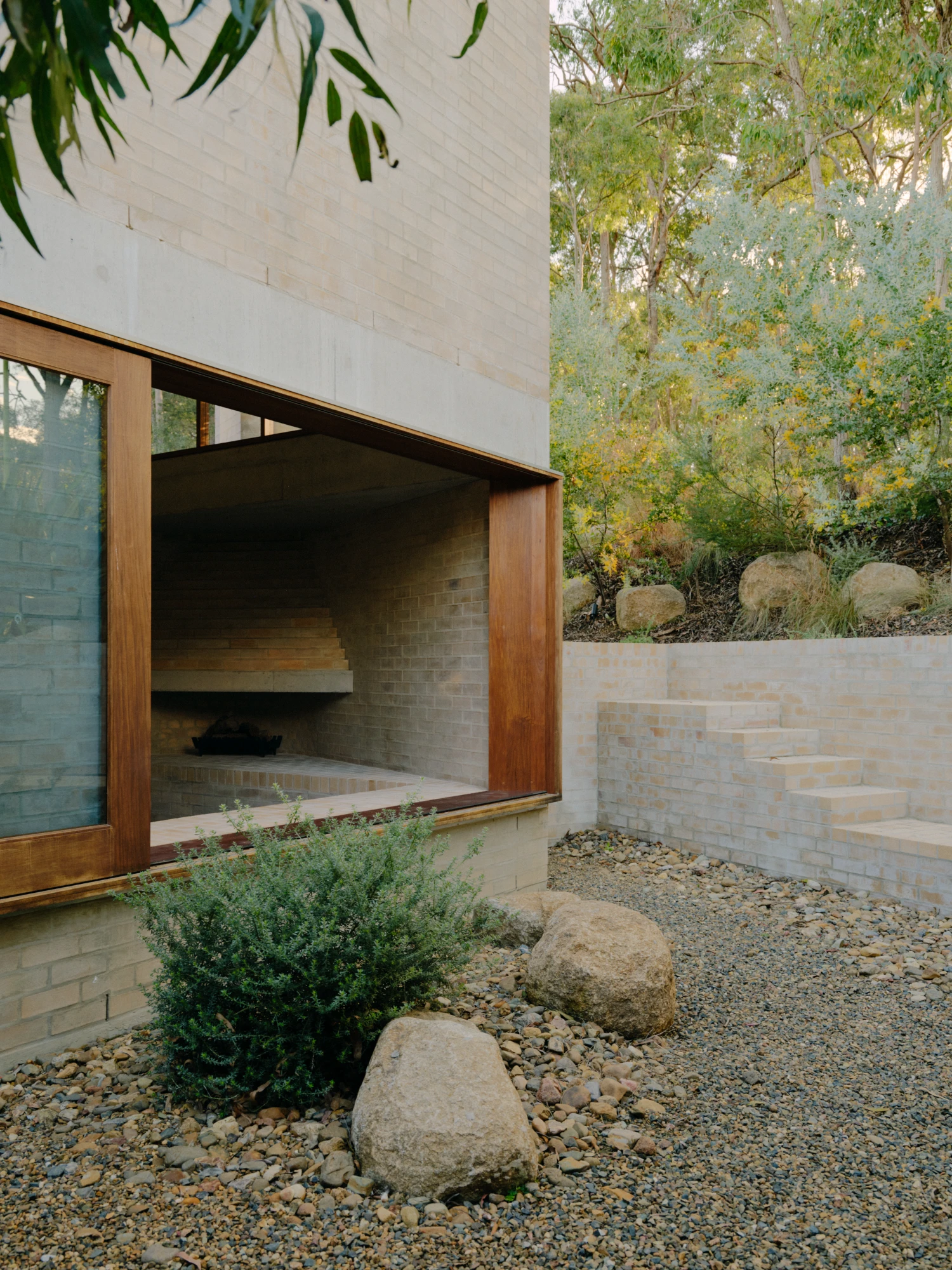 Stuartholme House by Nielsen Jenkins + Michael Lumby — A timber-framed aperture carved into cream brick opens onto a recessed fireplace hearth, its stepped brick face ascending in horizontal courses.