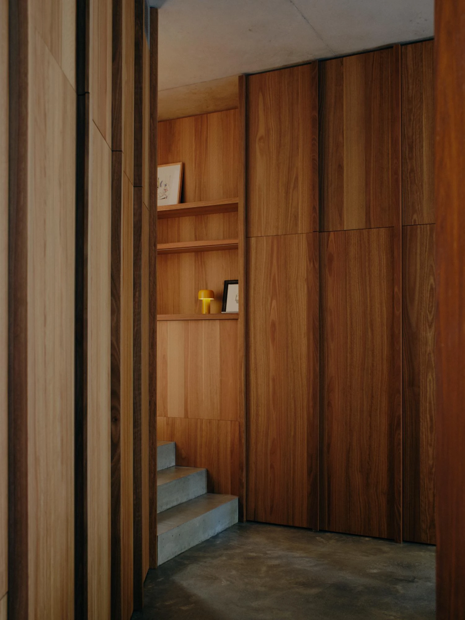 Stuartholme House by Nielsen Jenkins + Michael Lumby — A timber-lined passage descends into the house through a series of concrete steps, the space defined by vertical timber paneling in warm walnut tones.