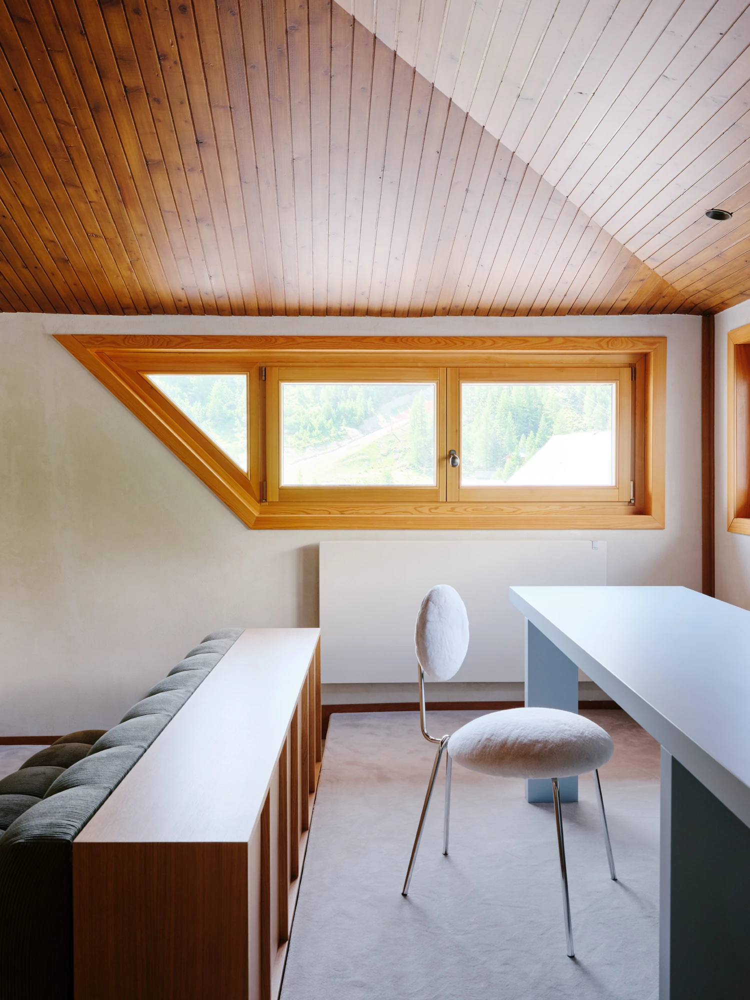 An Interior at Giomein by co.arch — A pitched attic room stripped to structural essentials, with a continuous timber-slat ceiling following the roof's angular geometry.
