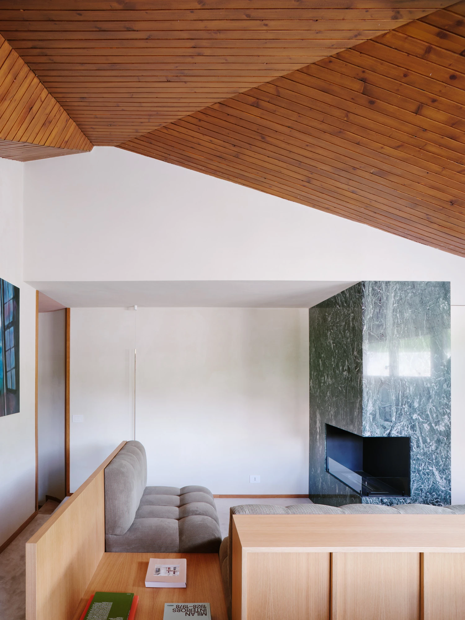 An Interior at Giomein by co.arch — The angled timber ceiling follows the pitched roof geometry, its parallel slats rendered in warm wood tones that establish the room's primary visual rhythm.
