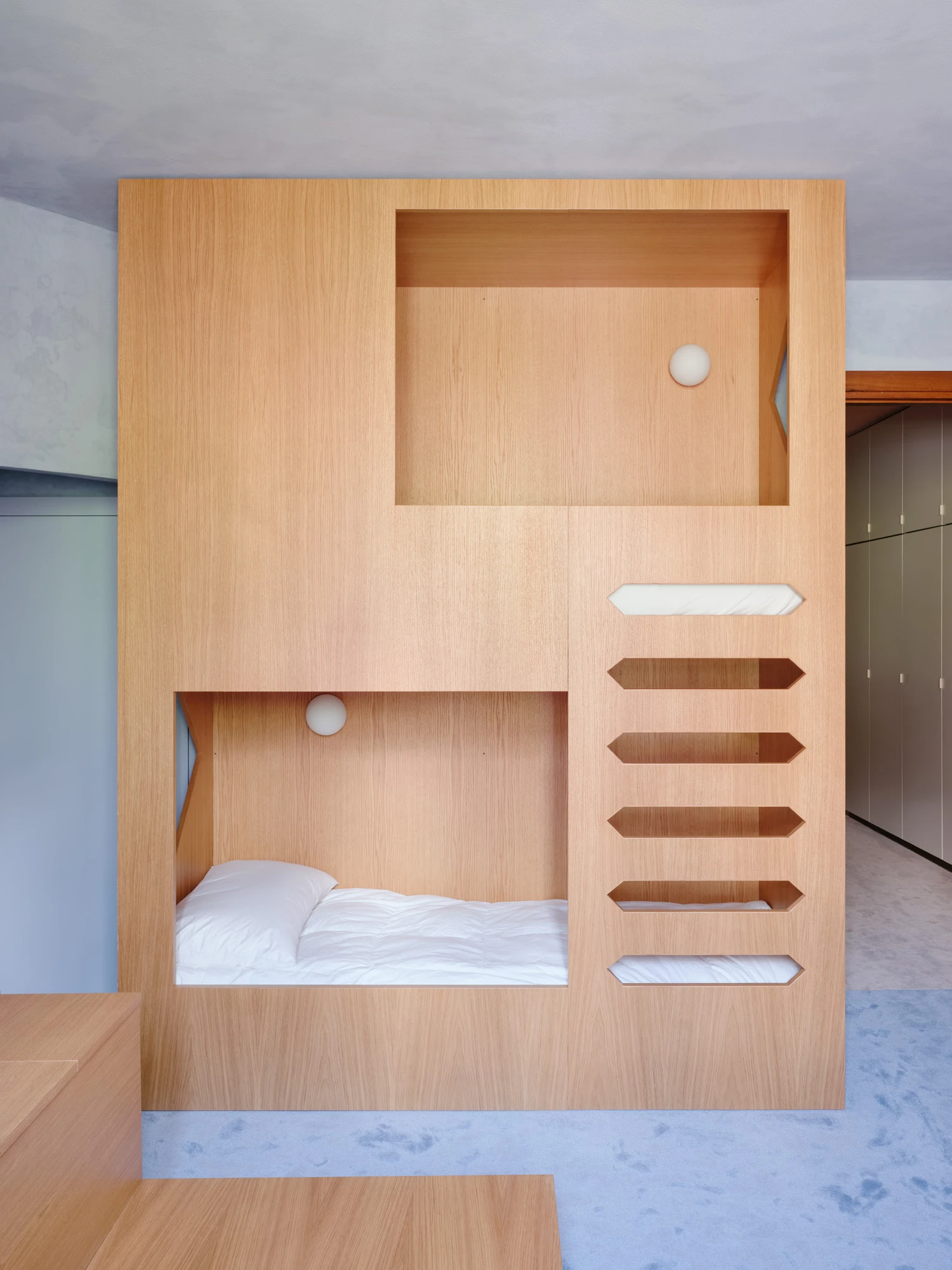 An Interior at Giomein by co.arch — A timber-clad built-in bed alcove occupies the lower left of a pine-veneered cubic structure, its white bedding visible within a recessed cavity.