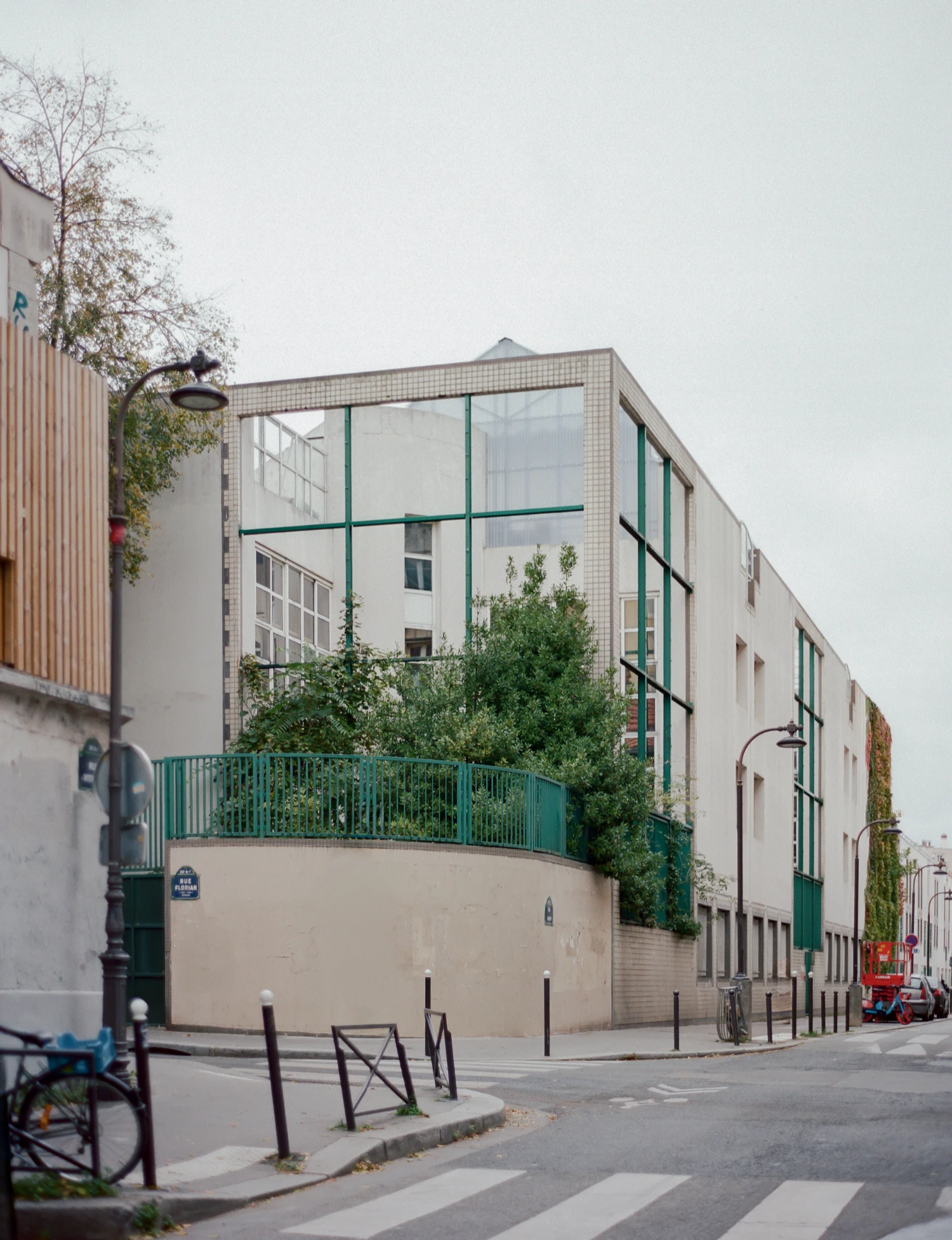 Rooftop Educational Farm by rerum architectes — The rooftop educational farm presents itself through a layered facade of green-framed glazing and cream render, establishing a transparent threshold between...