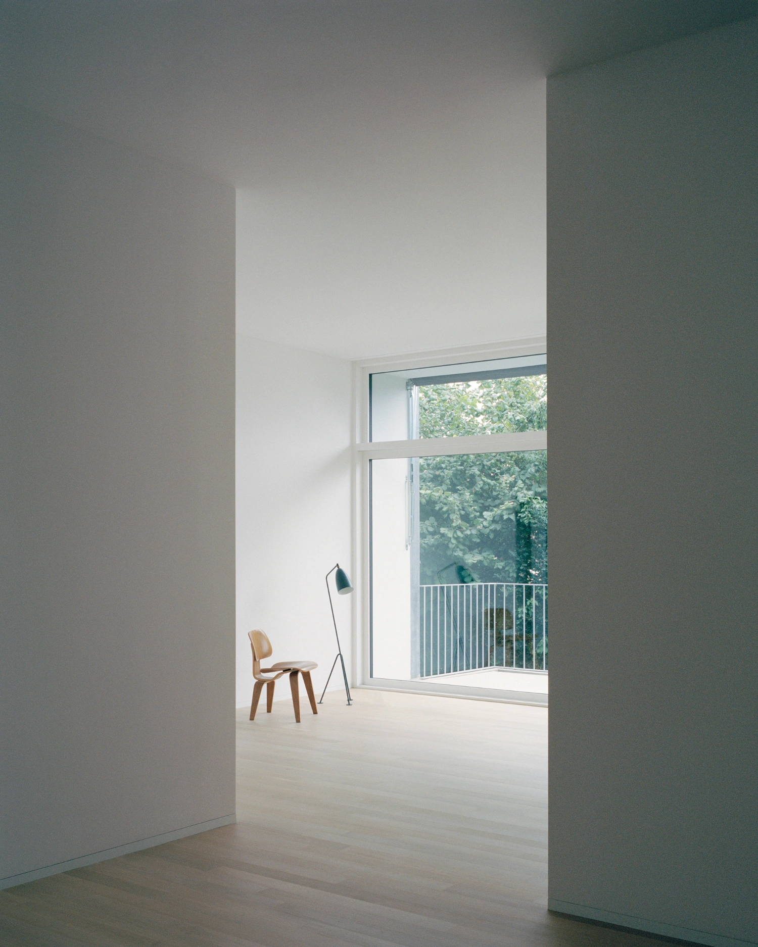 House on a Slope by KARAMUK KUO — A threshold view into a split-level interior space, framed by white-rendered walls and a deep doorway.