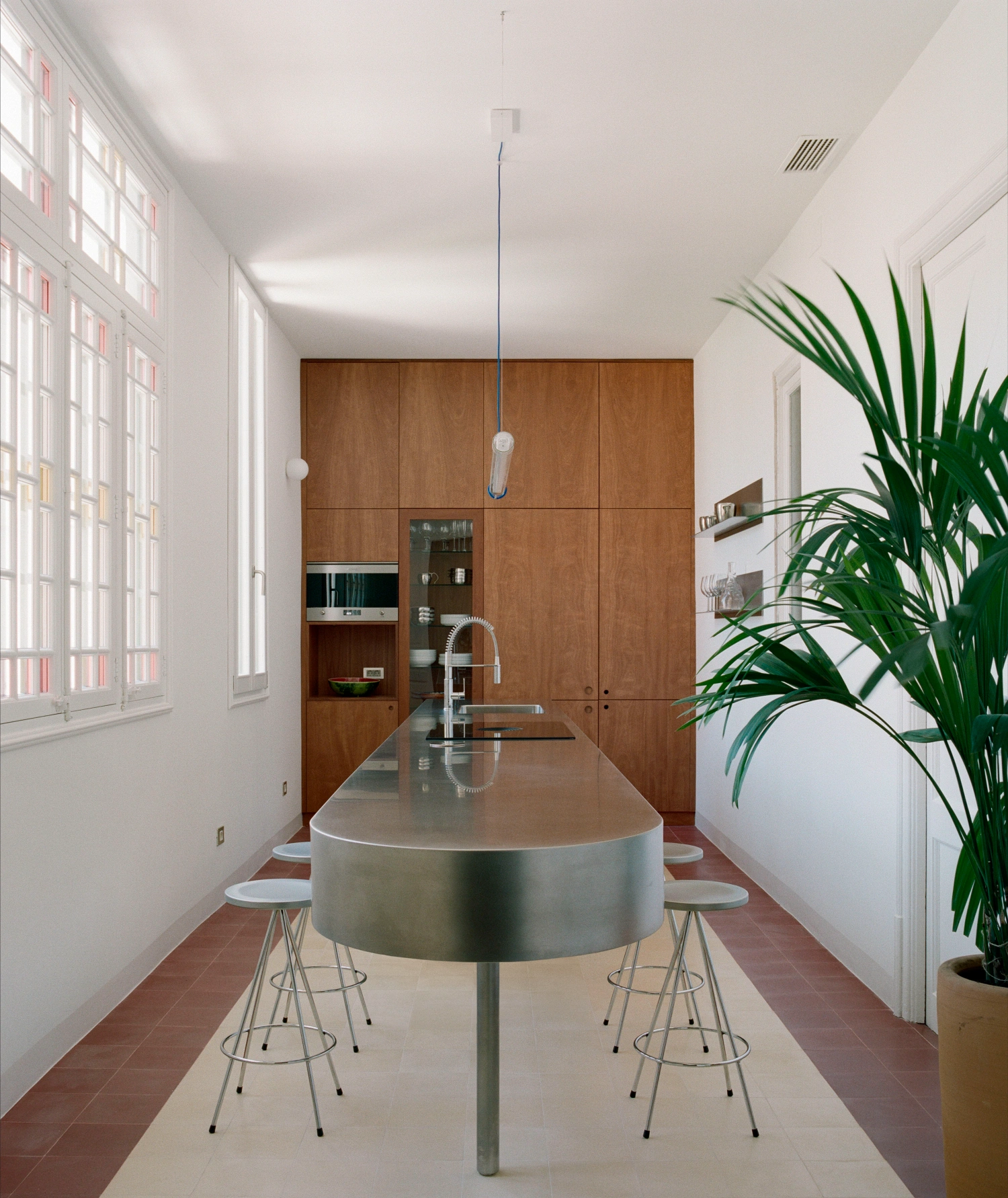 LL731 by Aramé Studio — A galley kitchen transformed into a social hub through a sculptural intervention: a monolithic steel-clad circular island anchors the narrow corridor...