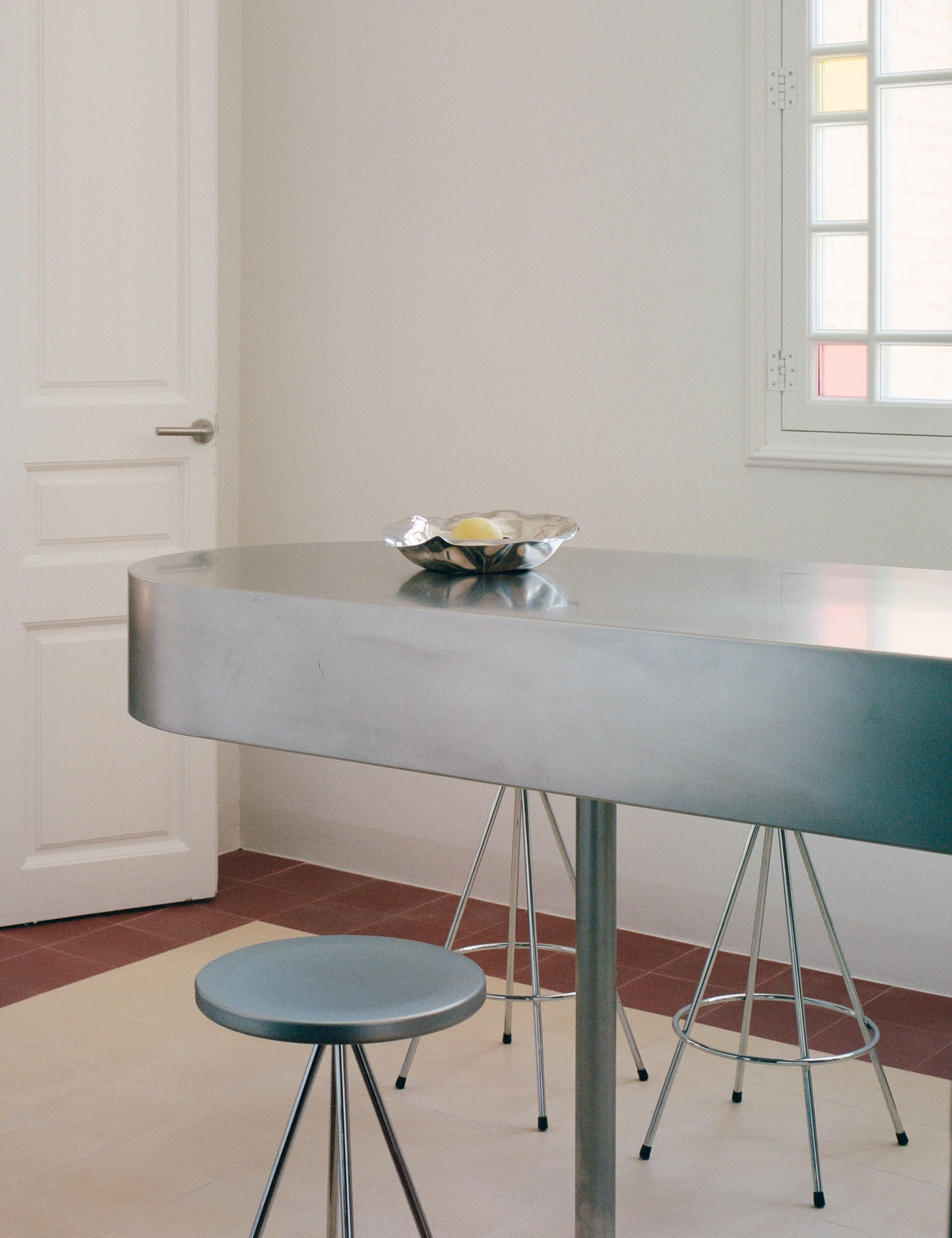LL731 by Aramé Studio — A minimalist dining zone anchored by a curved grey plaster table with a monolithic profile, supported by slender steel tripod legs.