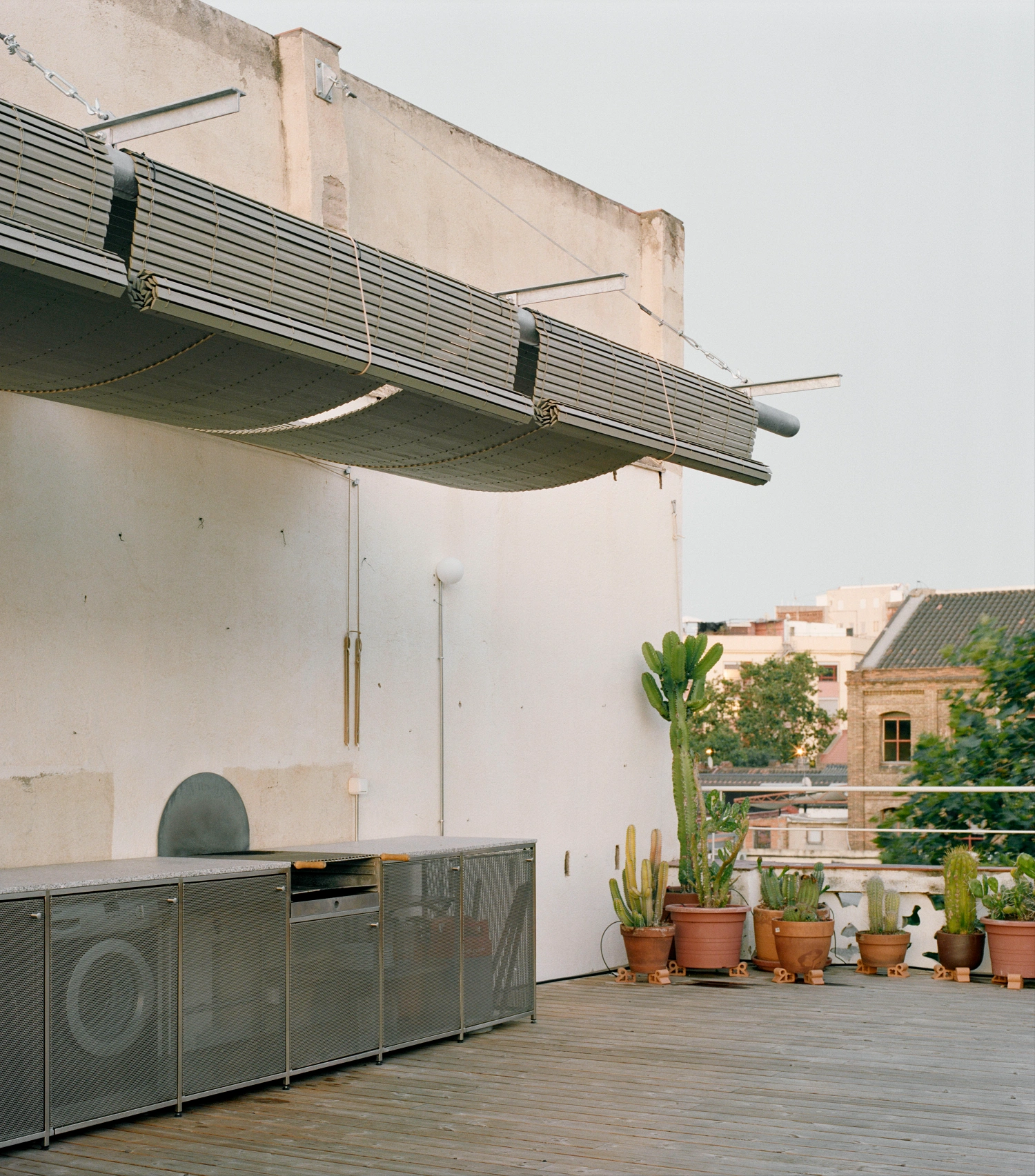 LL731 by Aramé Studio — A rooftop kitchen terrace in Barcelona overlooks neighboring buildings across a wooden deck.